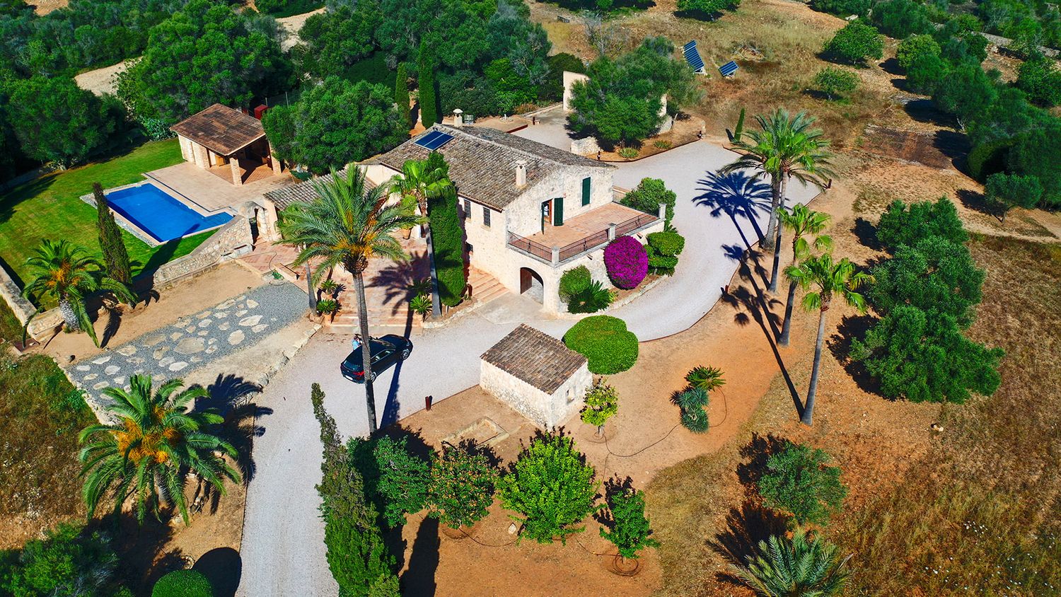 Aerial view of a Mediterranean villa complex with swimming pool and palm-lined driveway.
