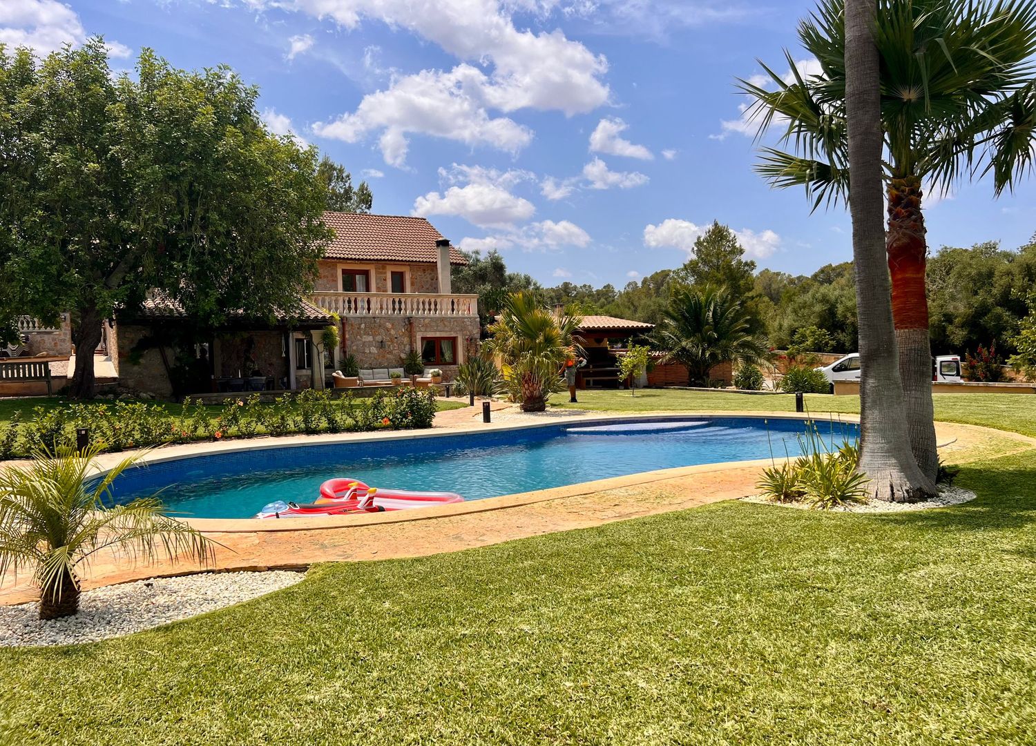 A panoramic view of a resort property with palm trees, swimming pool, and green lawn under bright blue skies.