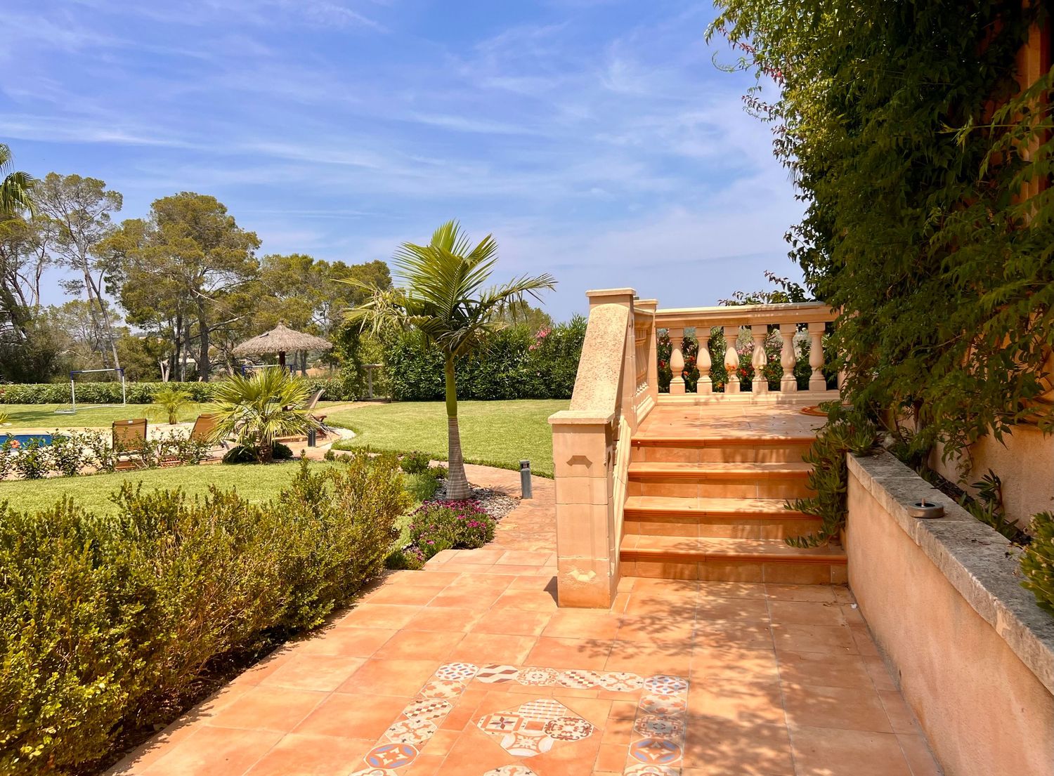 A panoramic view of a sunny residential terrace with terracotta tiles overlooking a lush green landscape and blue sky.