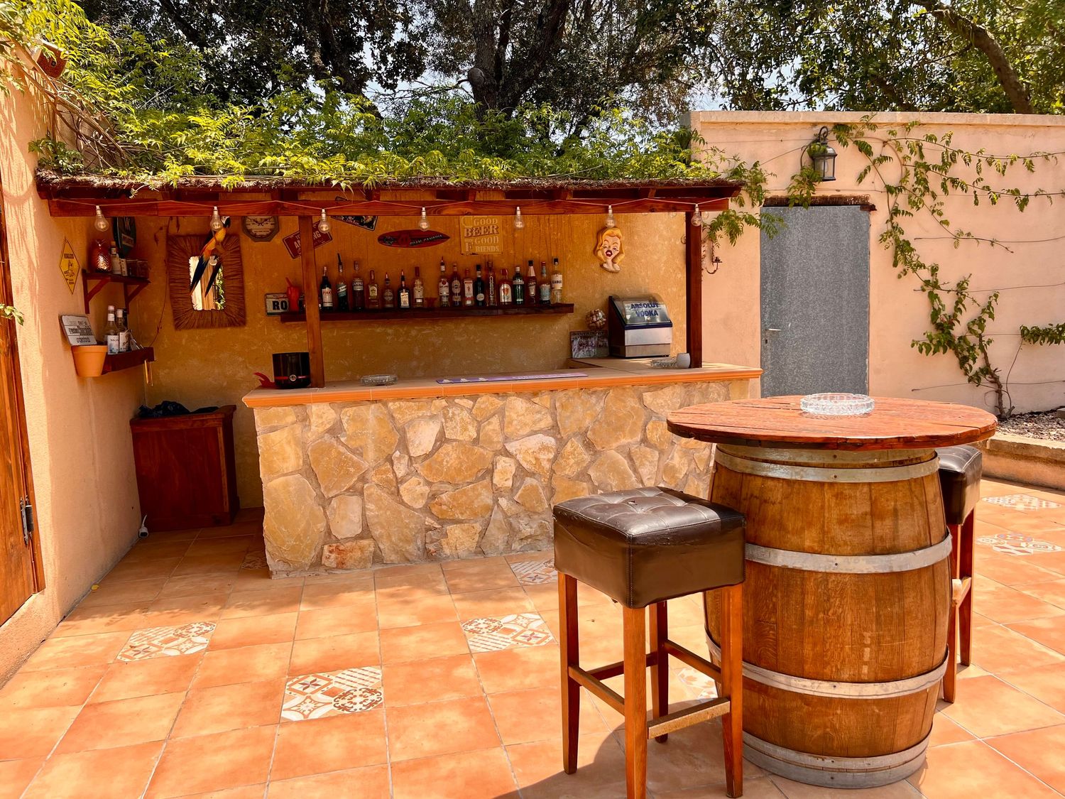 Rustic outdoor bar area with stone and terracotta features including wooden barrel tables and hanging copper pots.