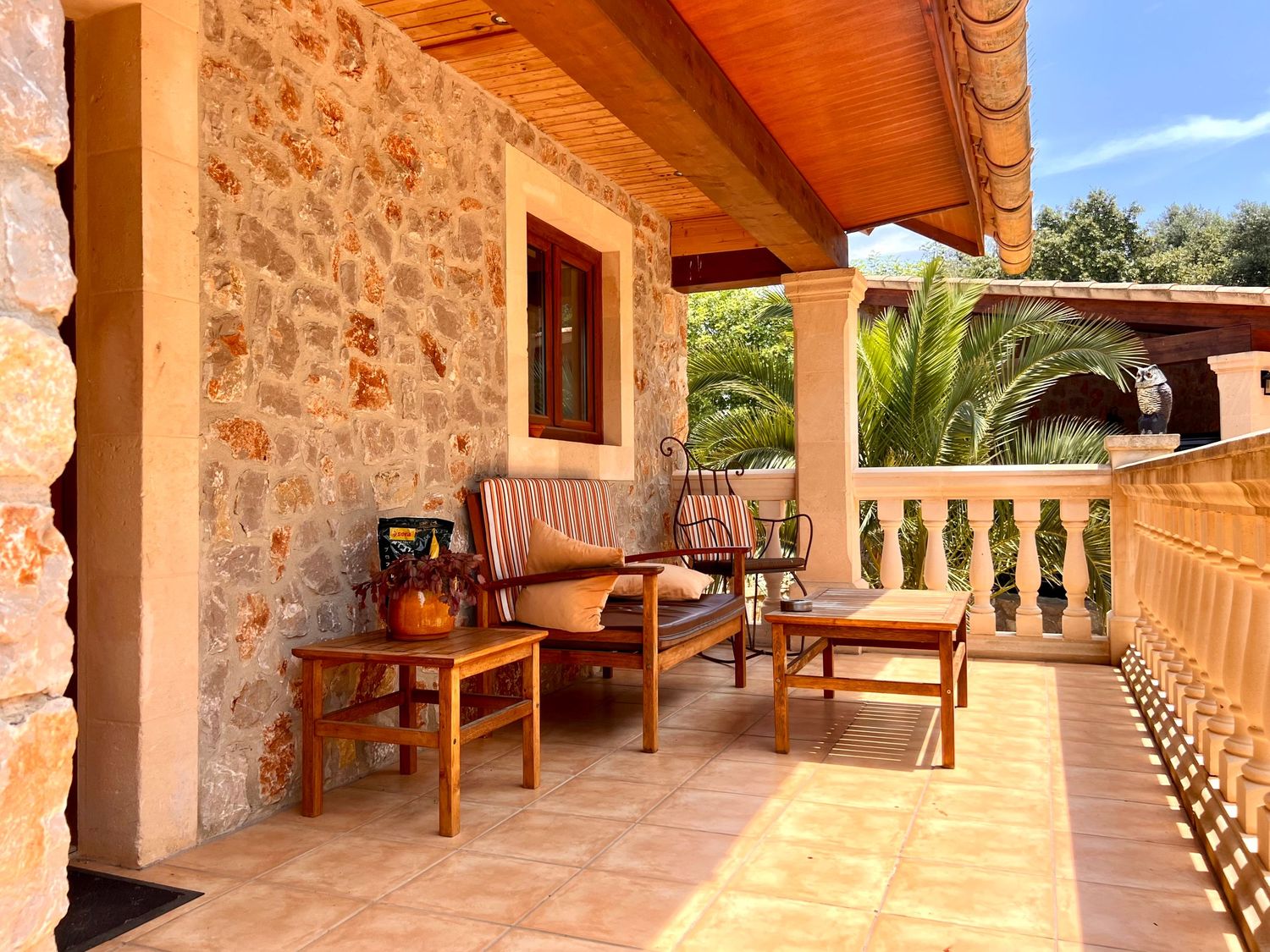 Stone patio with rustic wooden benches and Mediterranean decor creates a cozy outdoor seating area beneath a covered terrace.