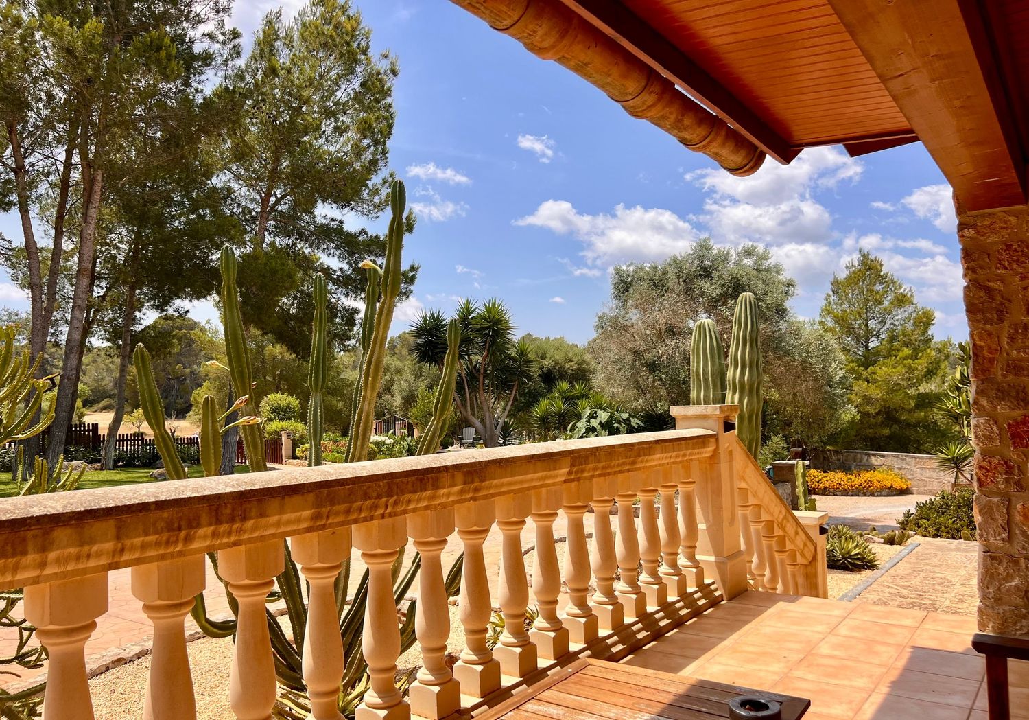 Mediterranean villa terrace with stone balustrade overlooking lush garden landscape on sunny day with blue skies.