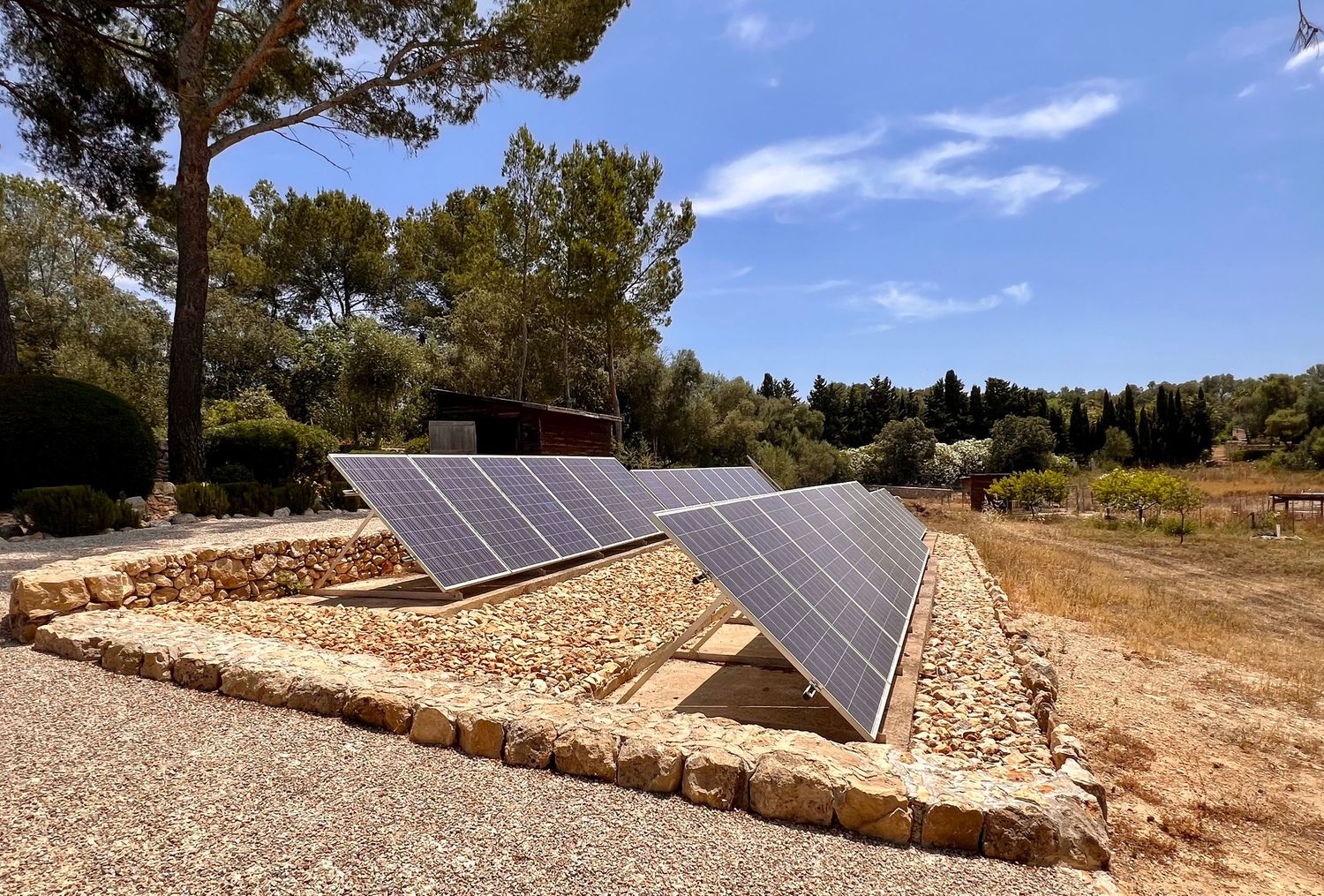 Solar panels installed along a rocky hillside terrain with trees and blue sky in the background.