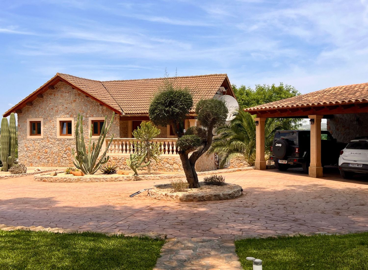Spanish style ranch home with stone facade, terra cotta roof tiles, covered carport and desert landscaping in front.