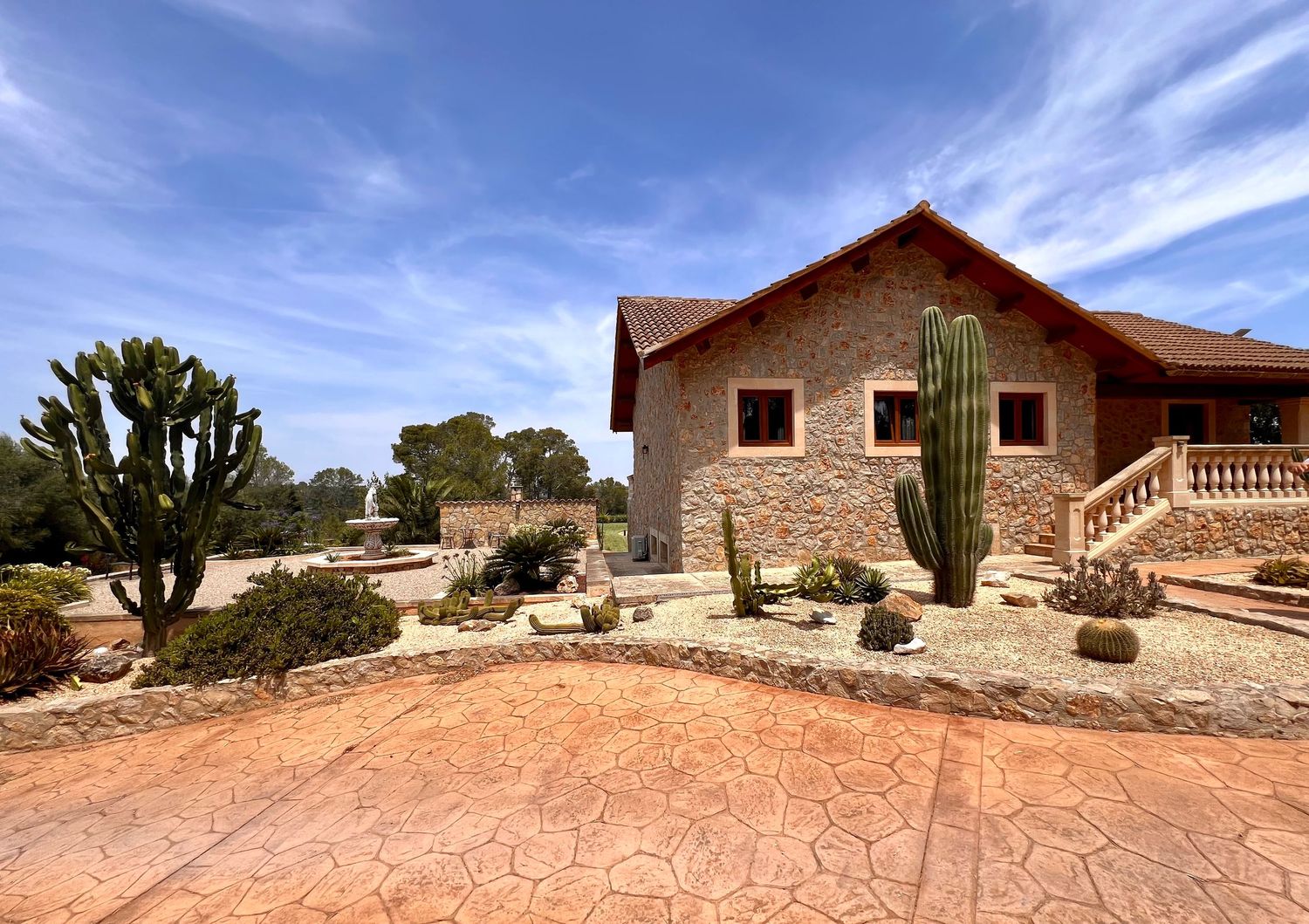 A rustic stone house with saguaro cactus and desert landscaping under a bright blue sky.