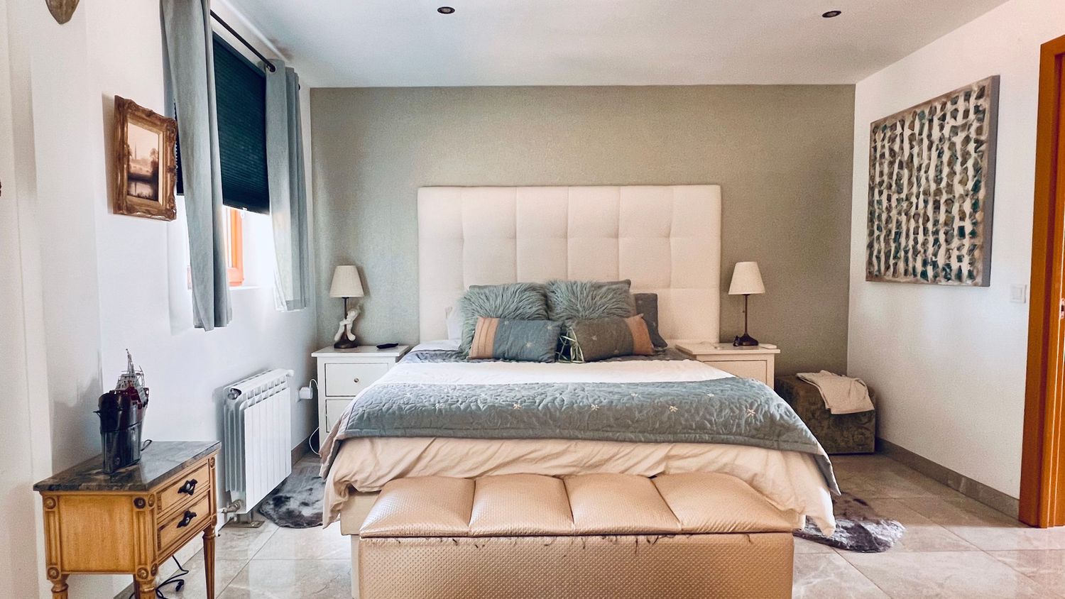 Modern bedroom with tufted headboard, blue accents, wooden side table and contemporary decor against light gray walls.