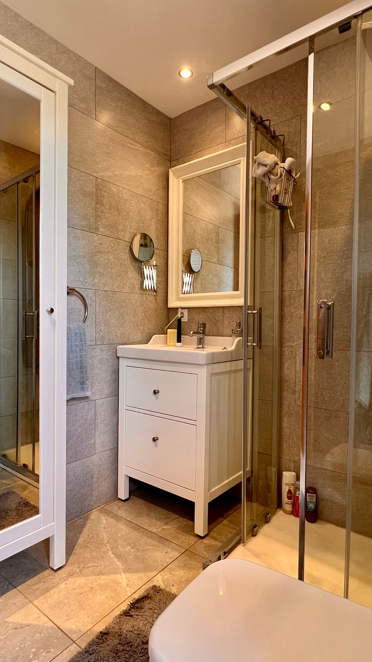 Modern bathroom interior with white vanity cabinet, glass shower enclosure and beige tile walls.