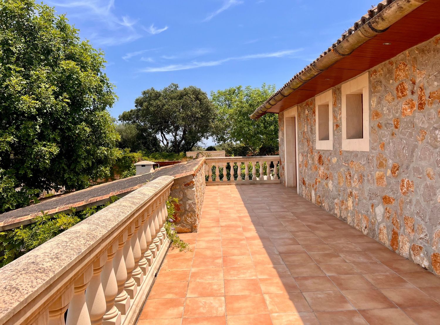 Mediterranean style terracotta balcony with stone balustrades overlooking scenic views under blue sky.