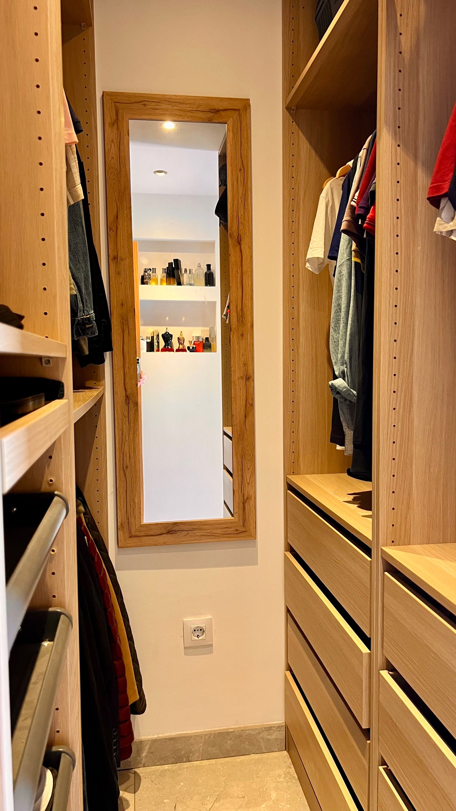Interior view of an organized walk-in closet with wooden shelving, drawers, and a full-length mirror mounted on the wall.