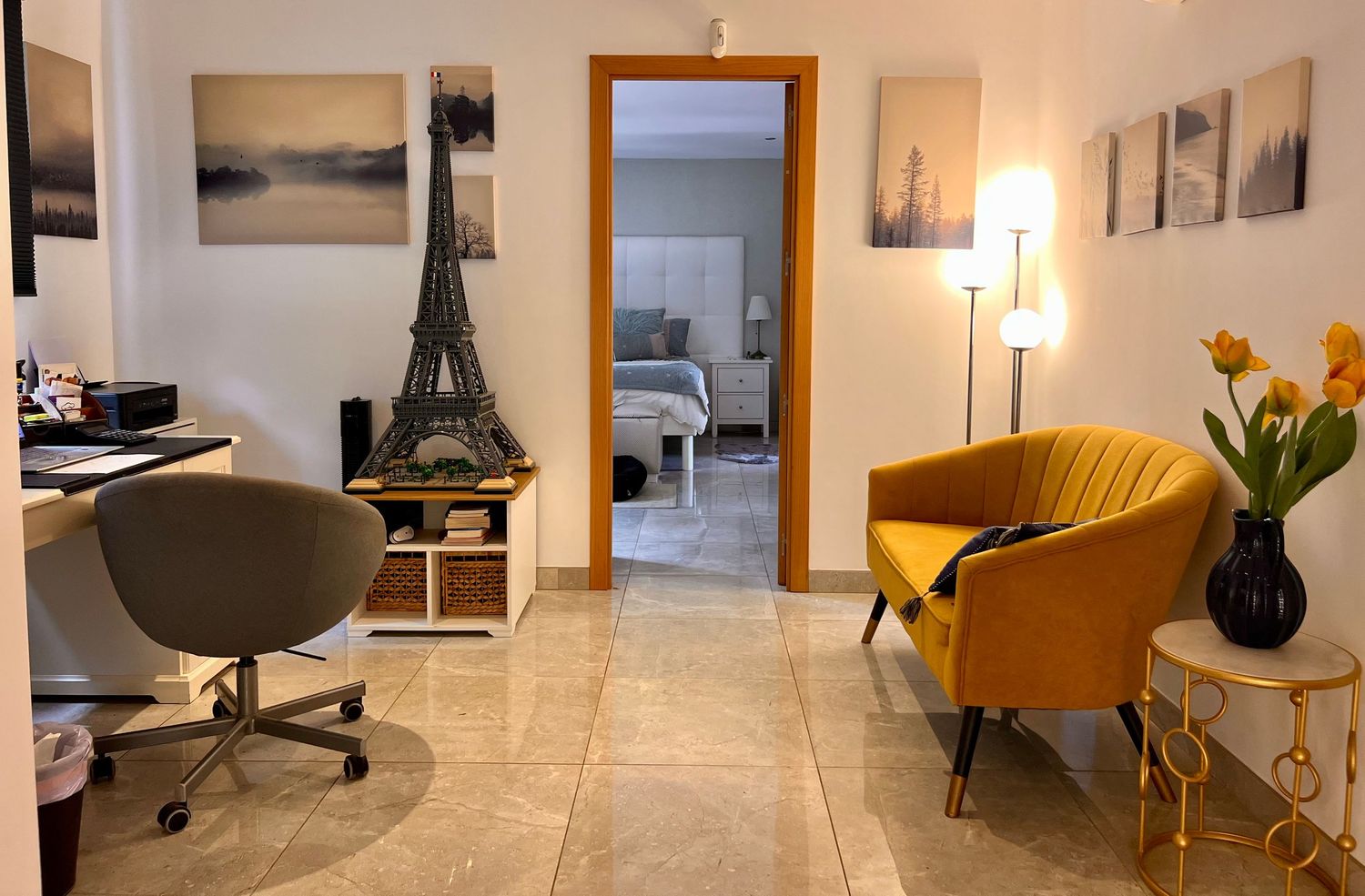 White marble flooring and modern minimalist decor create an elegant living space with warm lighting and yellow accent chairs.