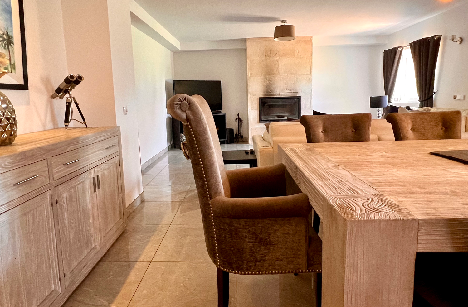 Modern dining area with rustic wooden table, brown upholstered chairs and white sideboard in open concept living space.