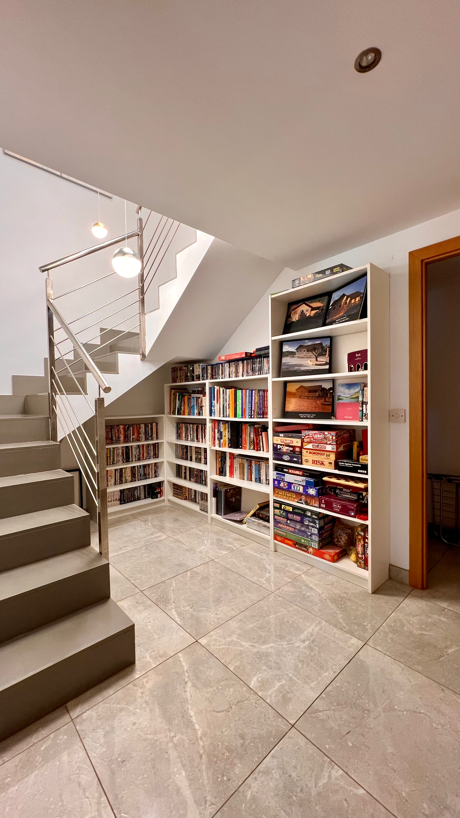 Modern basement staircase with stainless steel railings and built-in bookshelves filled with books and storage underneath.