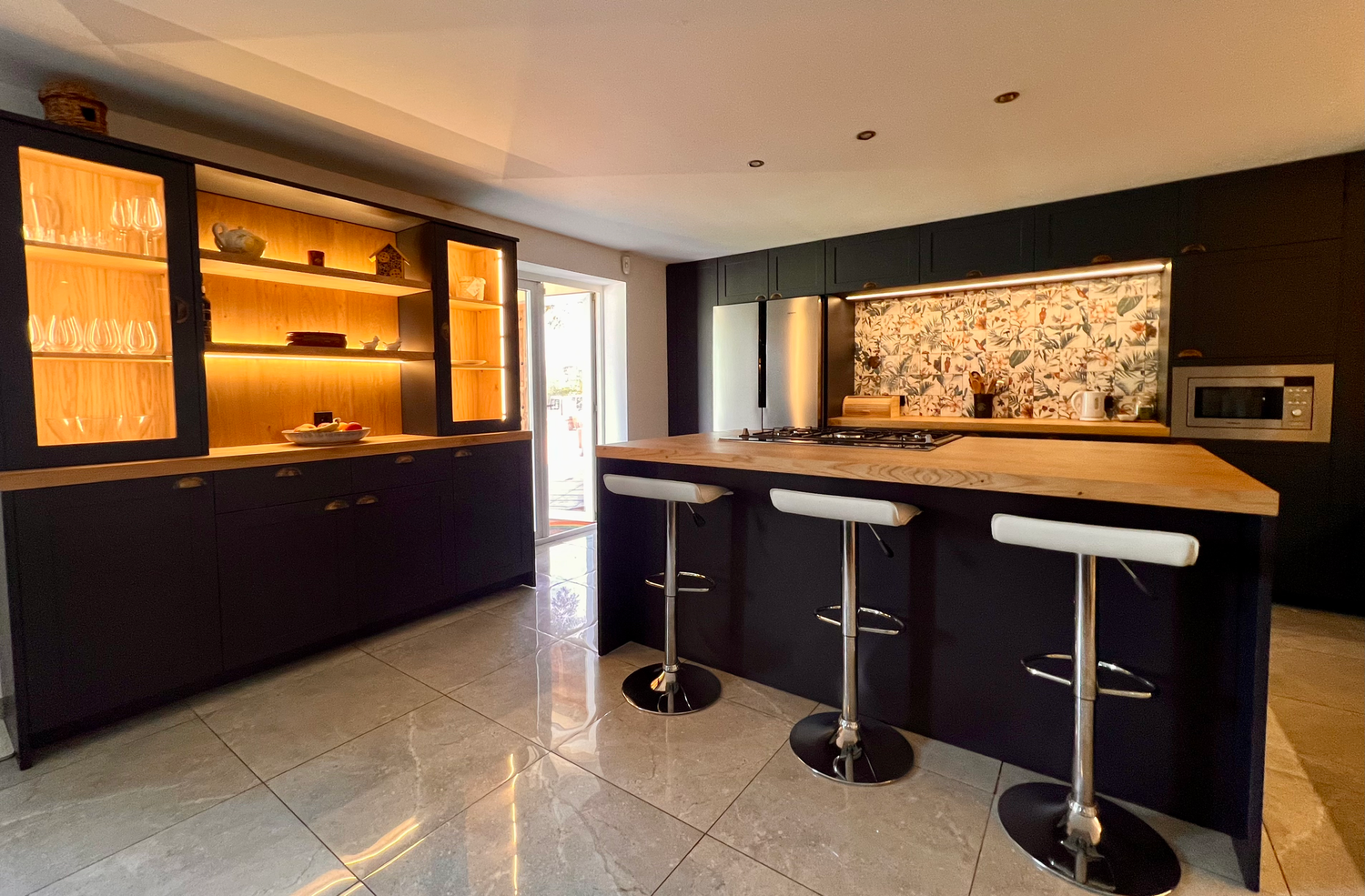 Contemporary home bar with dark cabinets, backlit shelving, and modern bar stools along a sleek counter.