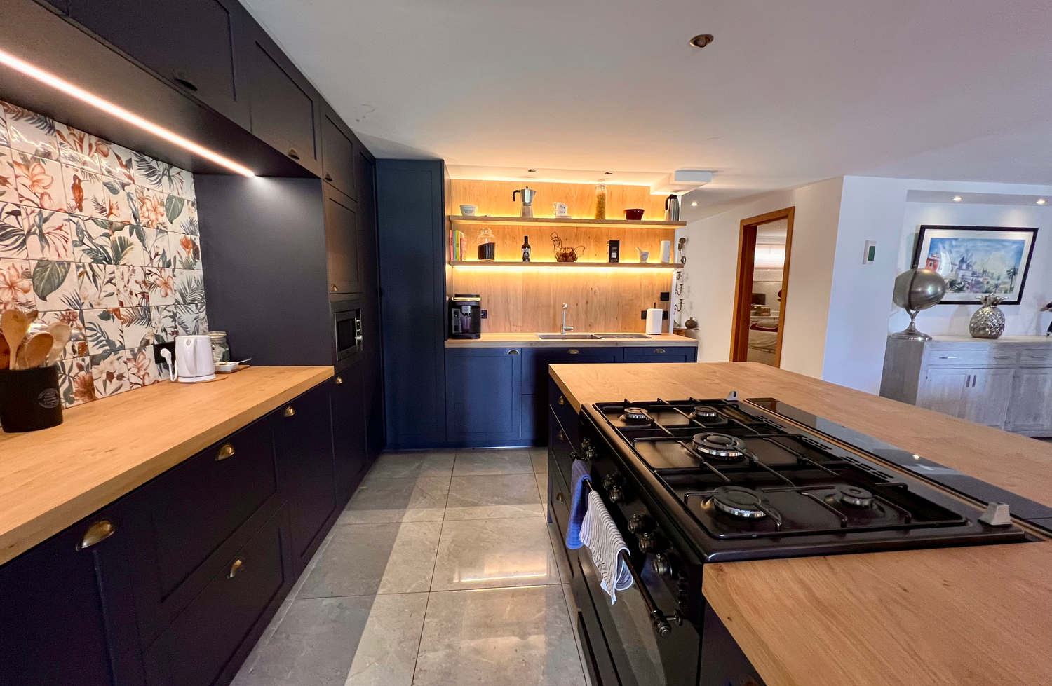 Modern kitchen interior with dark blue cabinets, wooden countertops and a central cooking island with gas stovetop.