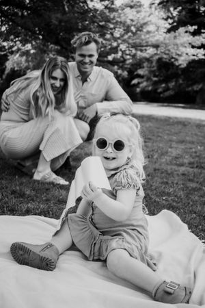 Girl with sunglasses on with parents laughing in the back.