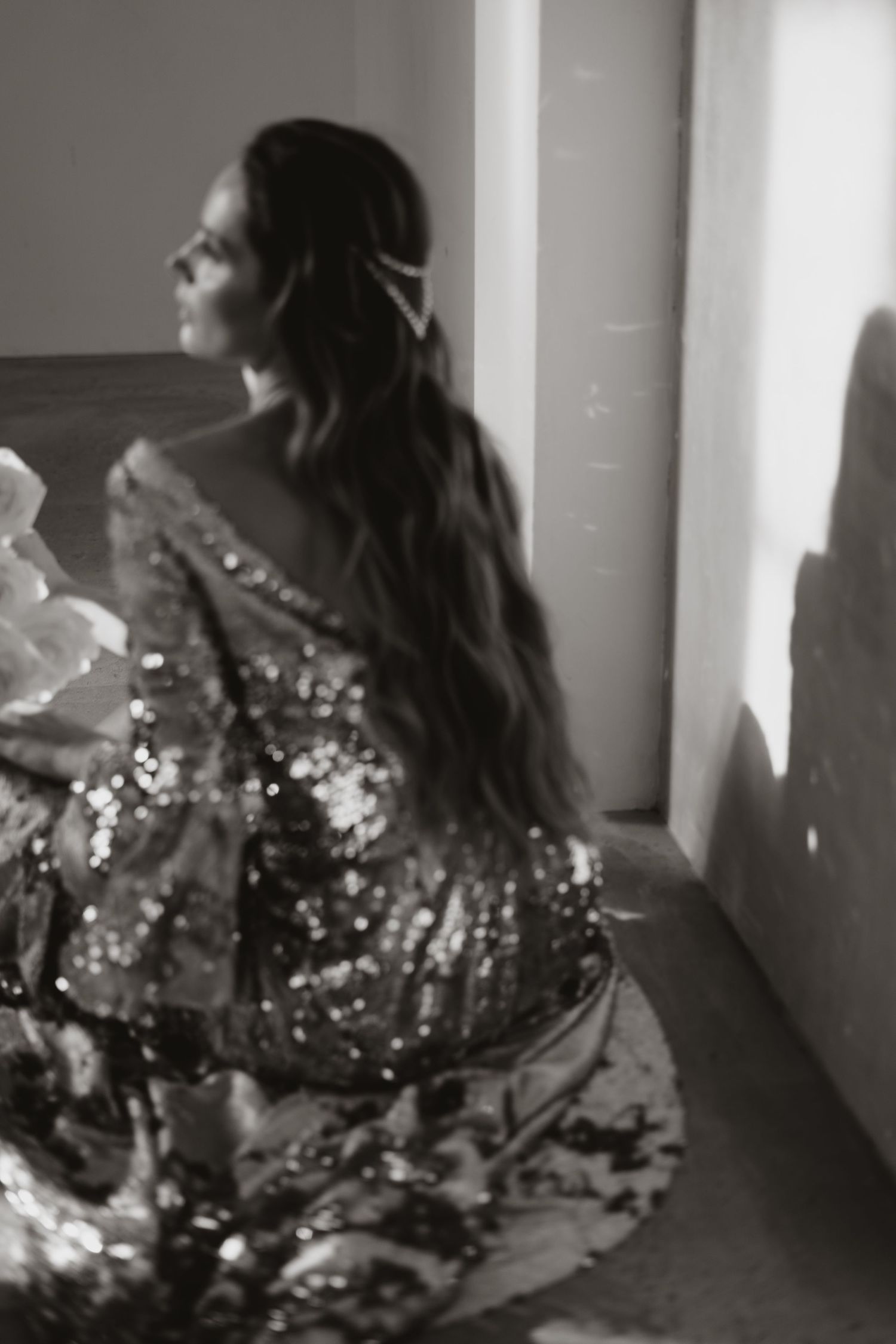 Side profile of a person in a sparkly dress sitting in dramatic lighting.