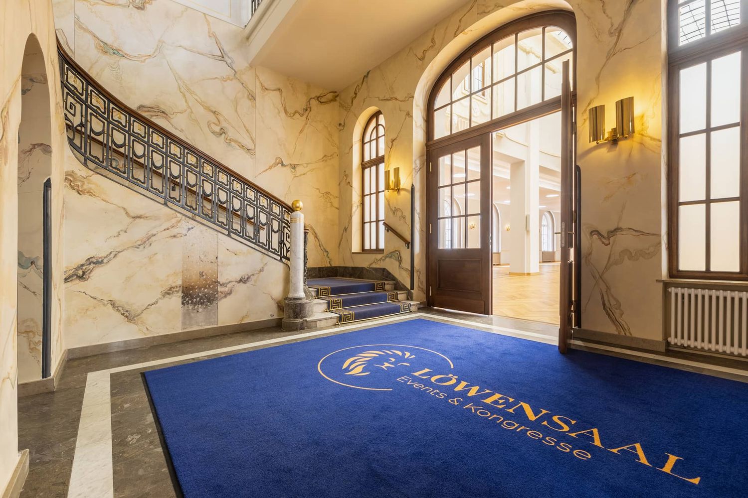 Ornate room with arched windows, marble details and royal blue carpeting showing classical design.