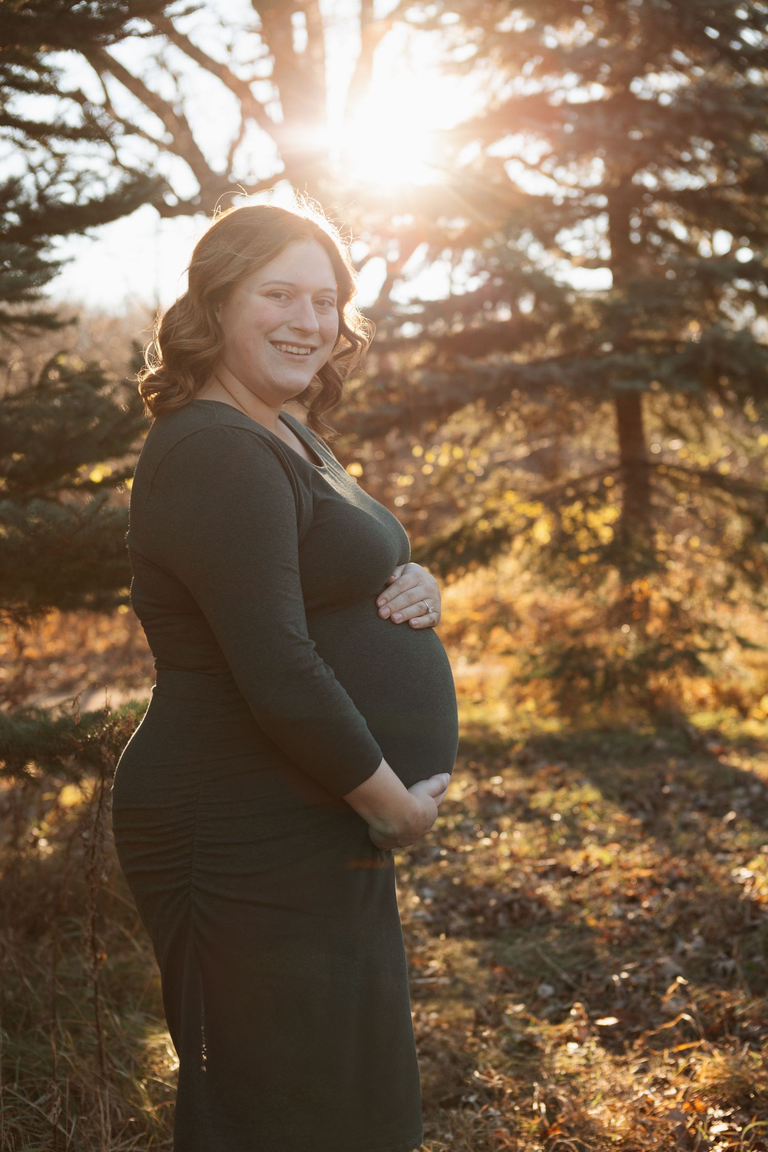 Maternity photos captured in golden sunlight with evergreen trees in background.