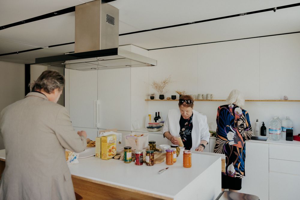 Modern white kitchen with people gathering around a counter with food and drinks.