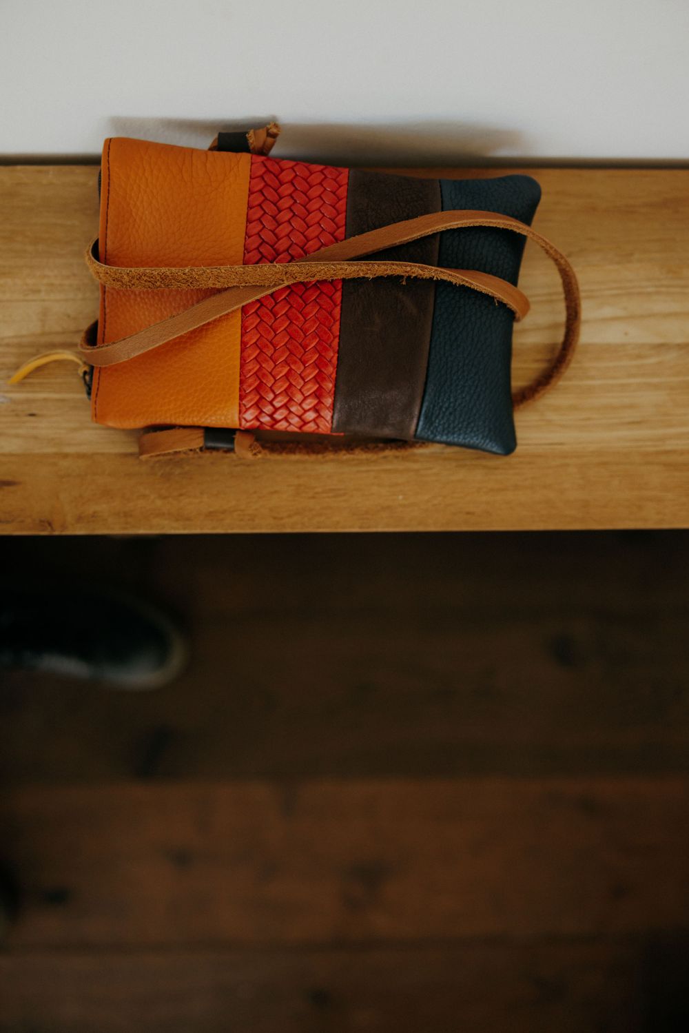 Colorful leather wallet with woven red detail displayed on wooden surface.
