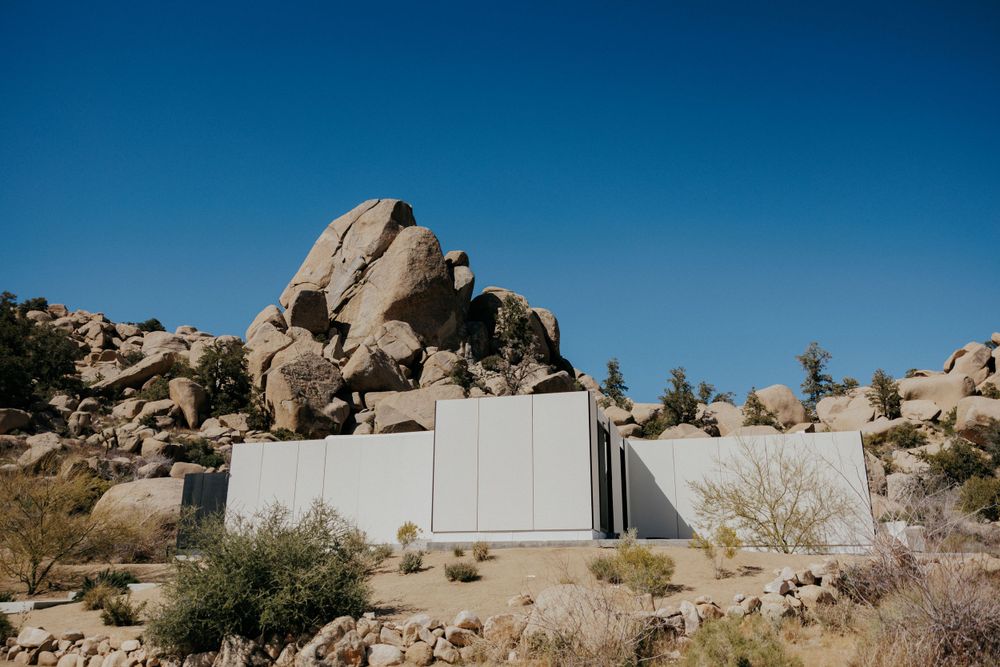 White modern structure built against large desert rock formations under blue sky.