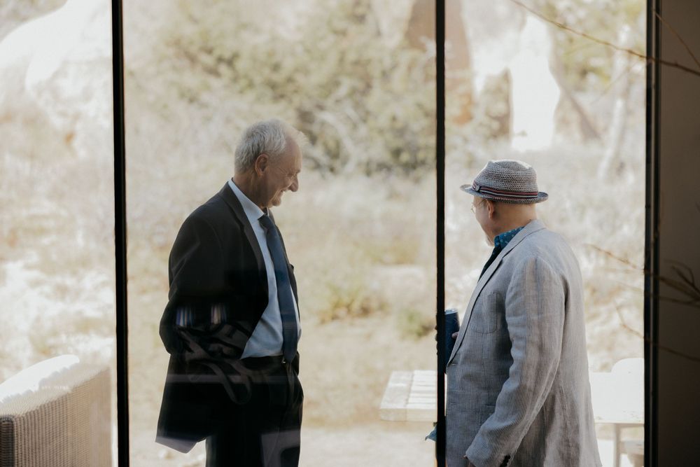 Two people in conversation silhouetted against bright outdoor window.