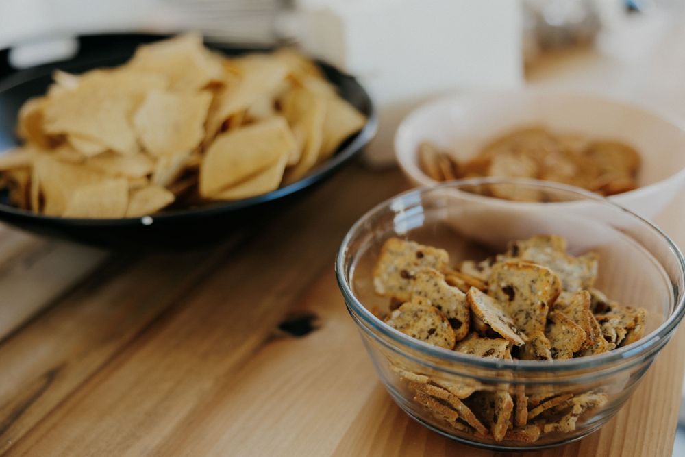 Bowls of chips and snacks arranged on wooden table surface.