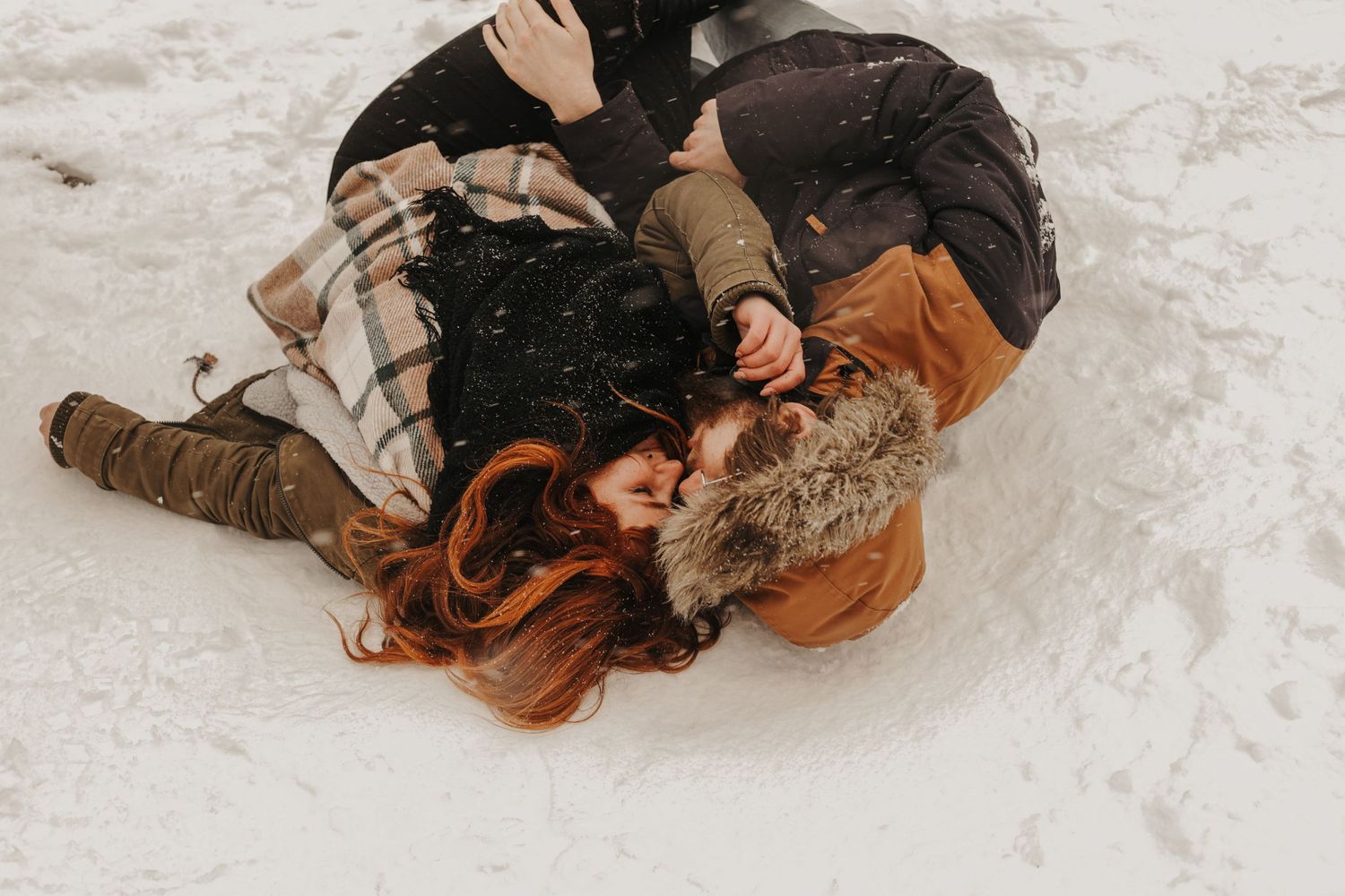 Couple lying in snow sharing intimate winter moment together.