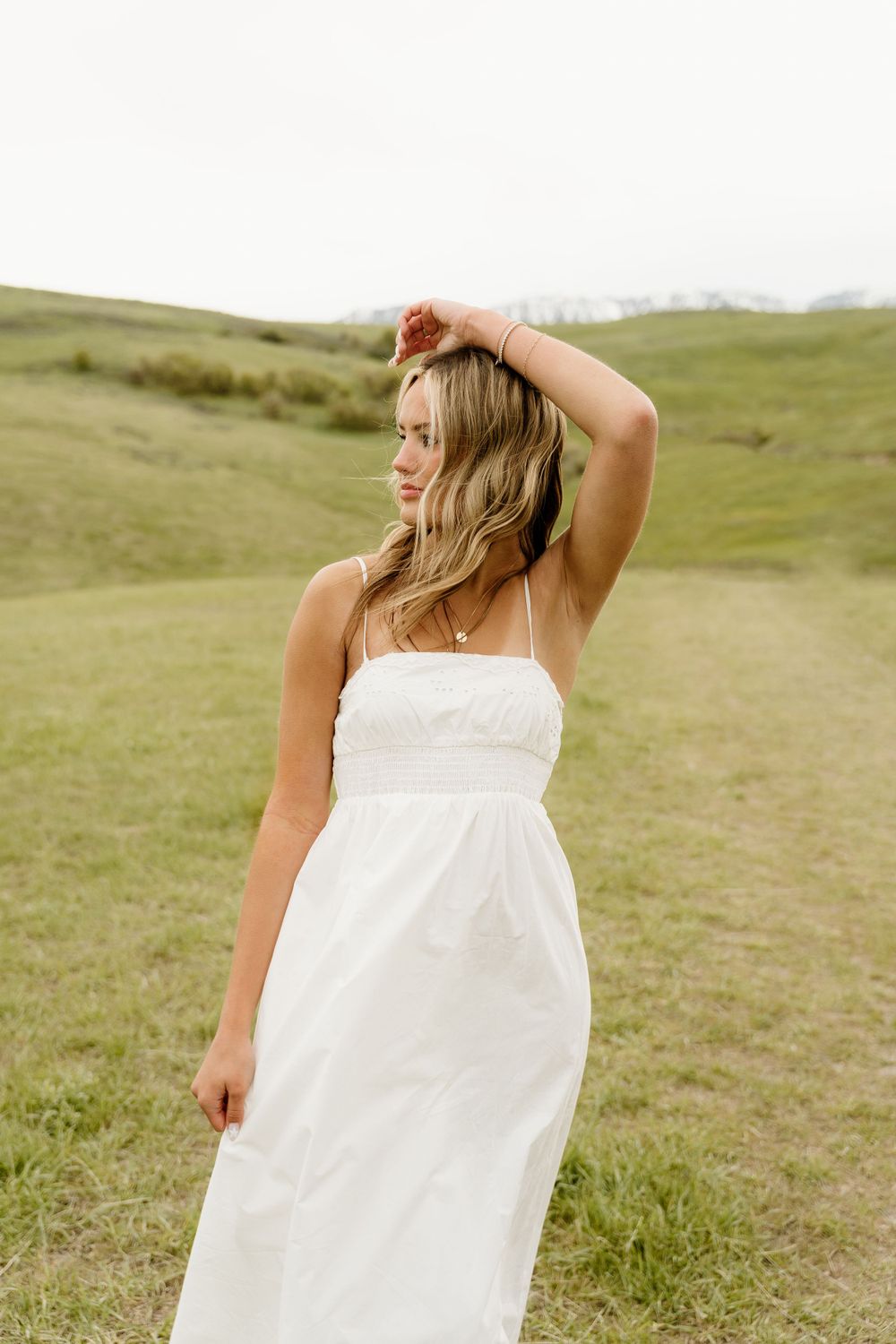 Graceful pose in a flowing white sundress amidst green rolling hills.