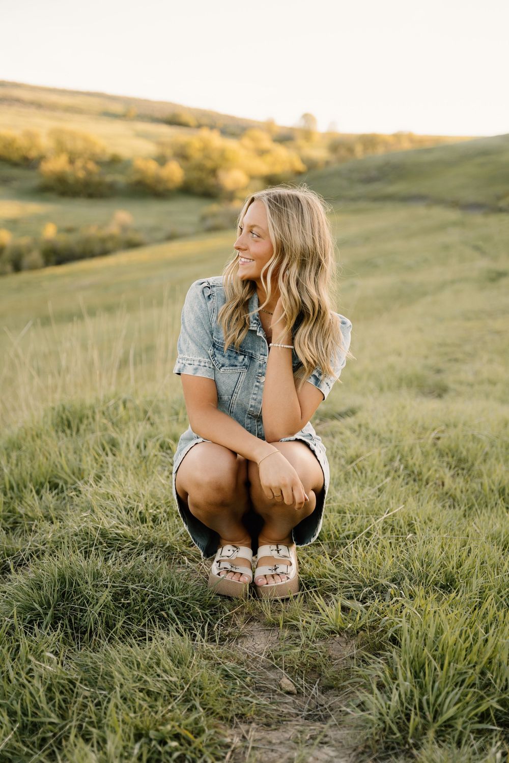 Casual summer portrait in denim outfit among tall grass at sunset.