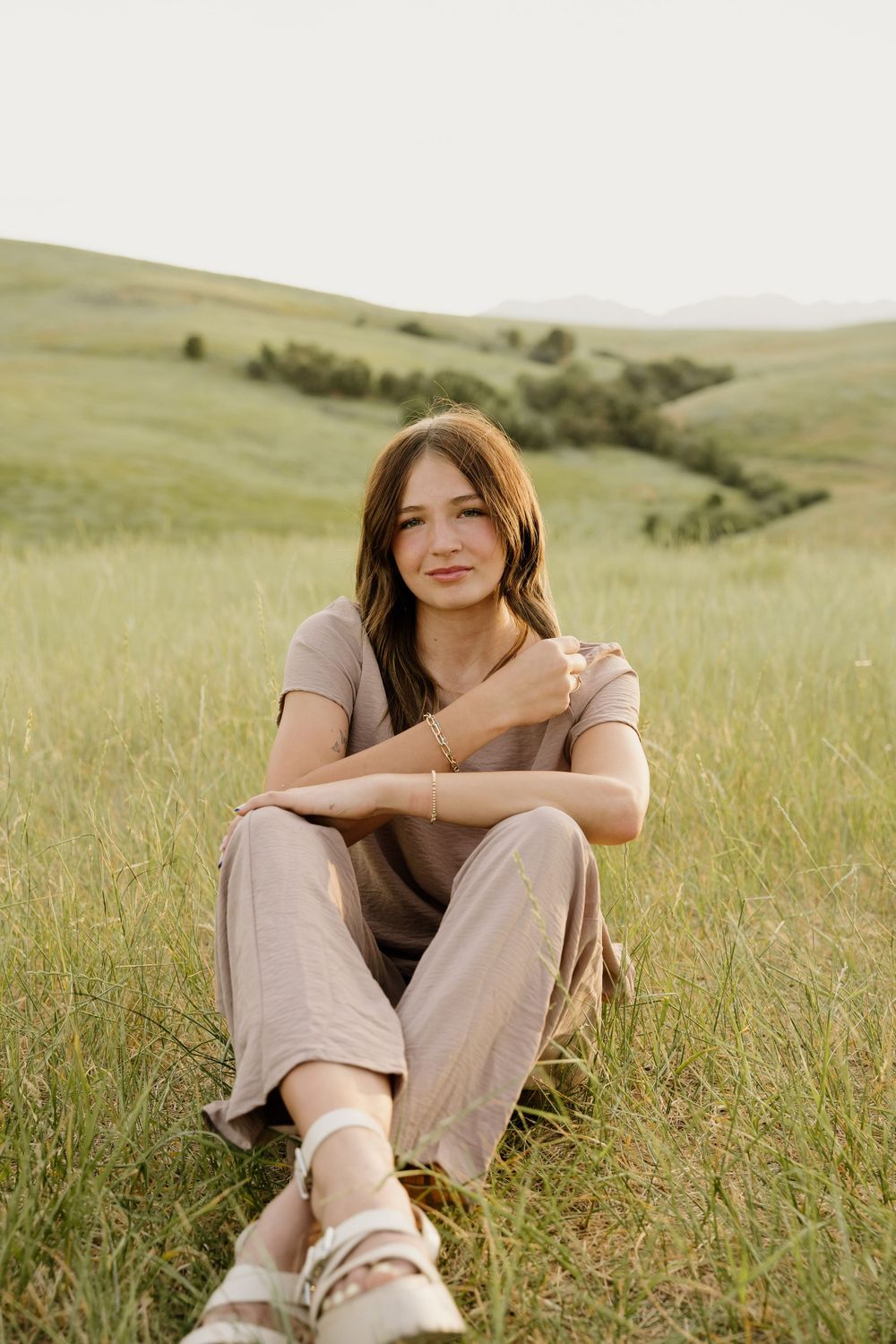 A casual portrait in neutral tones set against golden hillsides during sunset.