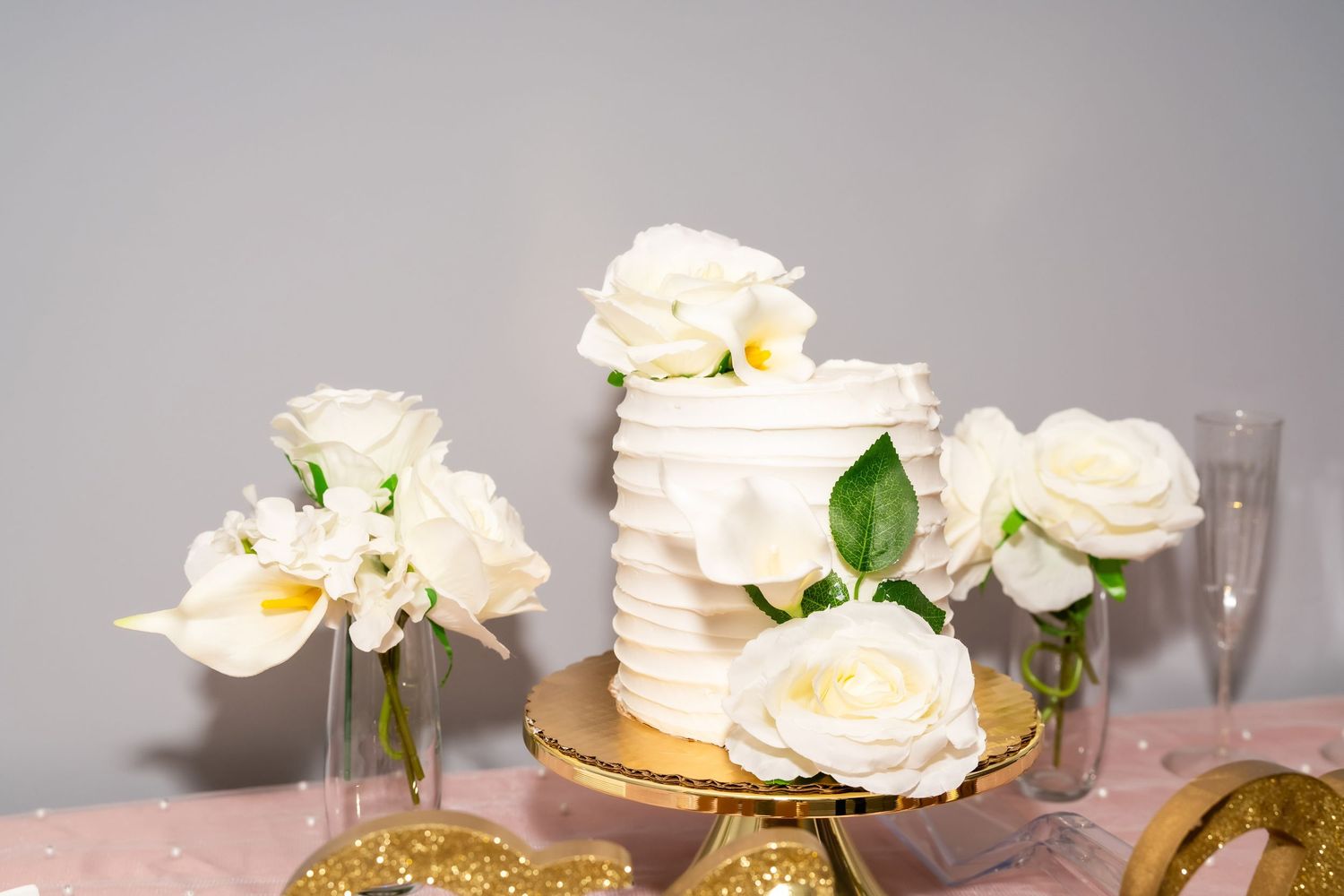 Wedding ceremony setup with wooden chiavari chairs and white backdrop with pink draping and floral arrangements.