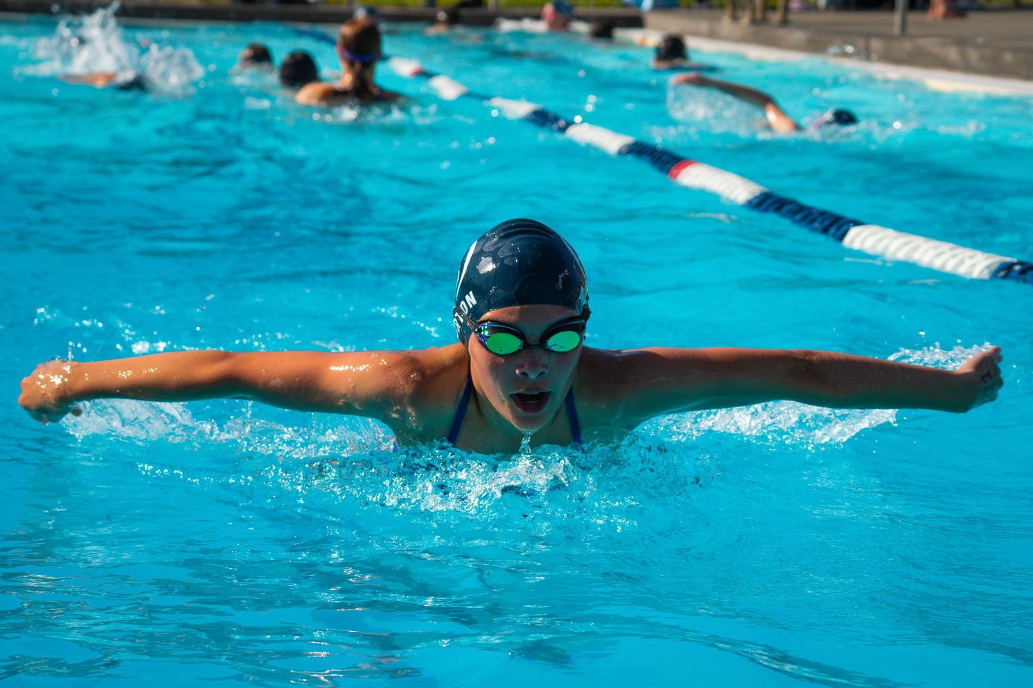 Swimmer performing butterfly stroke in bright blue swimming pool during practice session.