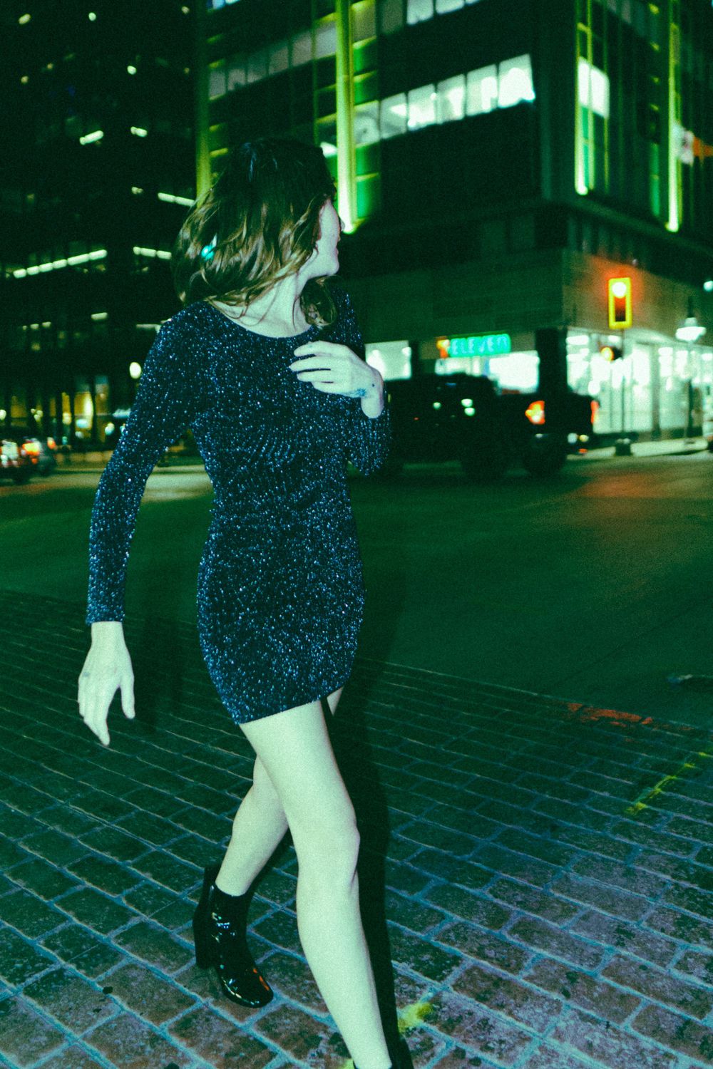 Figure in sparkling dress dances on cobblestone street at night.