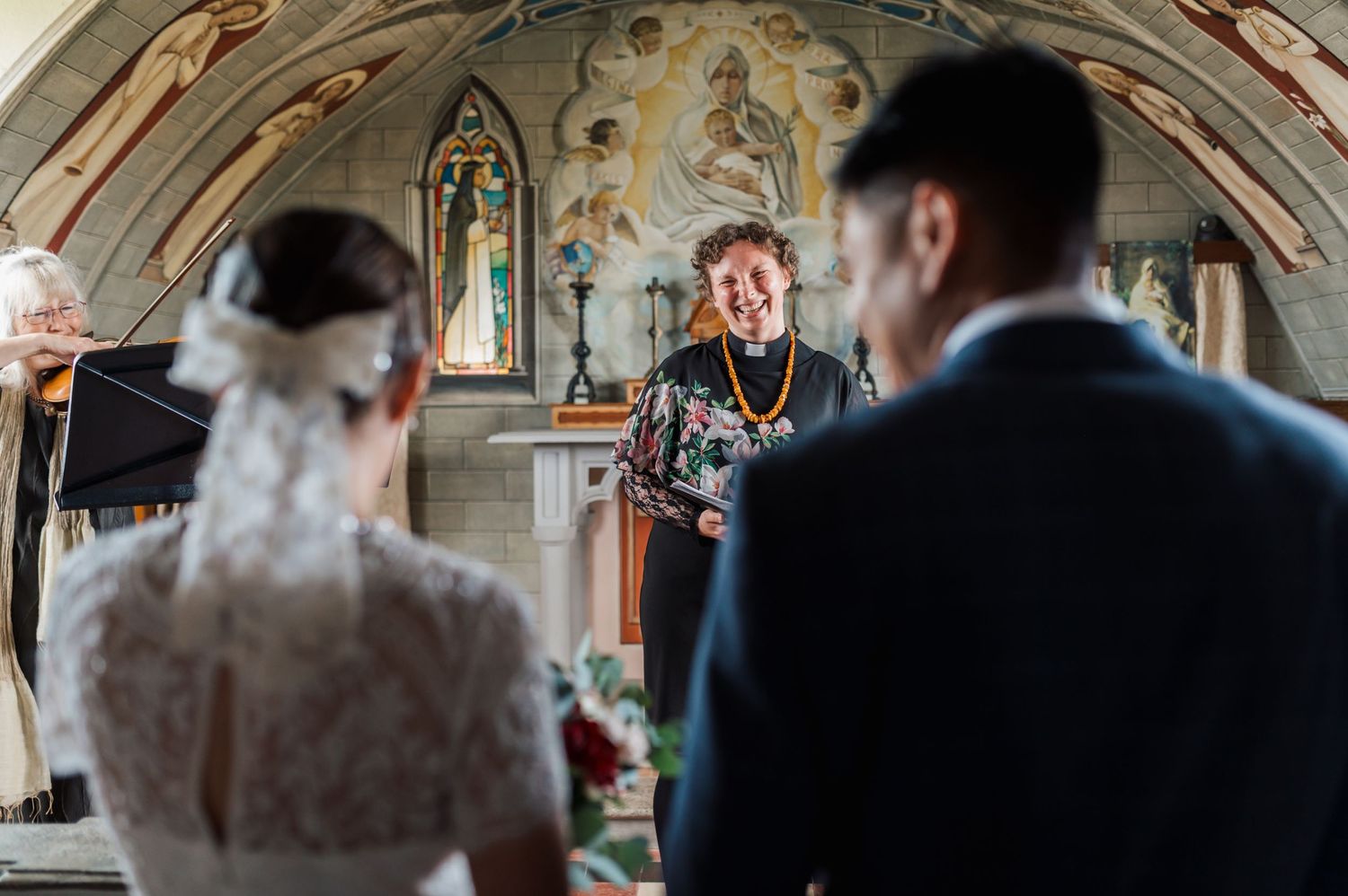 Officiant conducts wedding ceremony in historic chapel with painted religious frescoes on the walls.