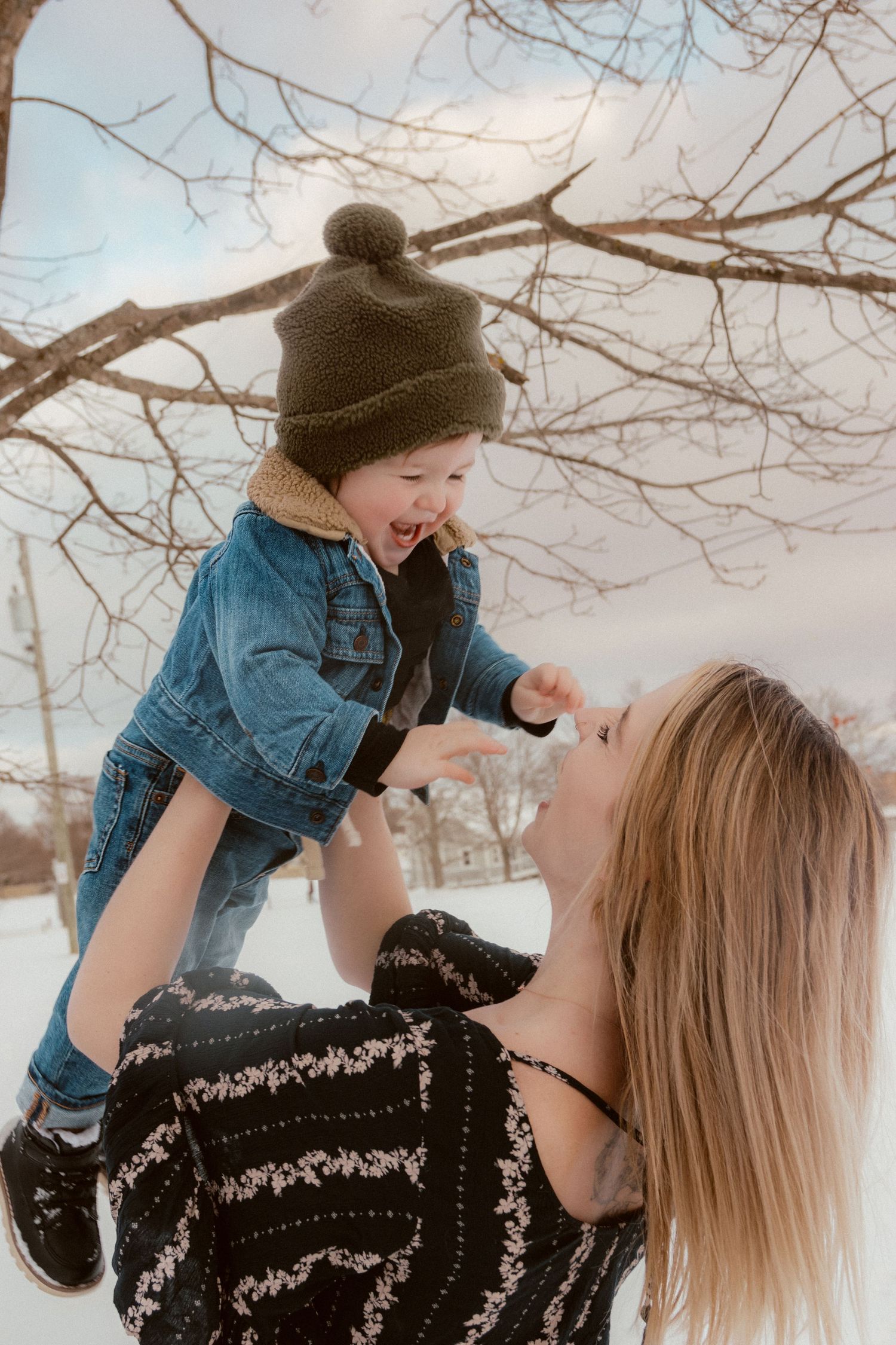 A joyful winter moment between adult and child playing beneath bare tree branches in the snow.