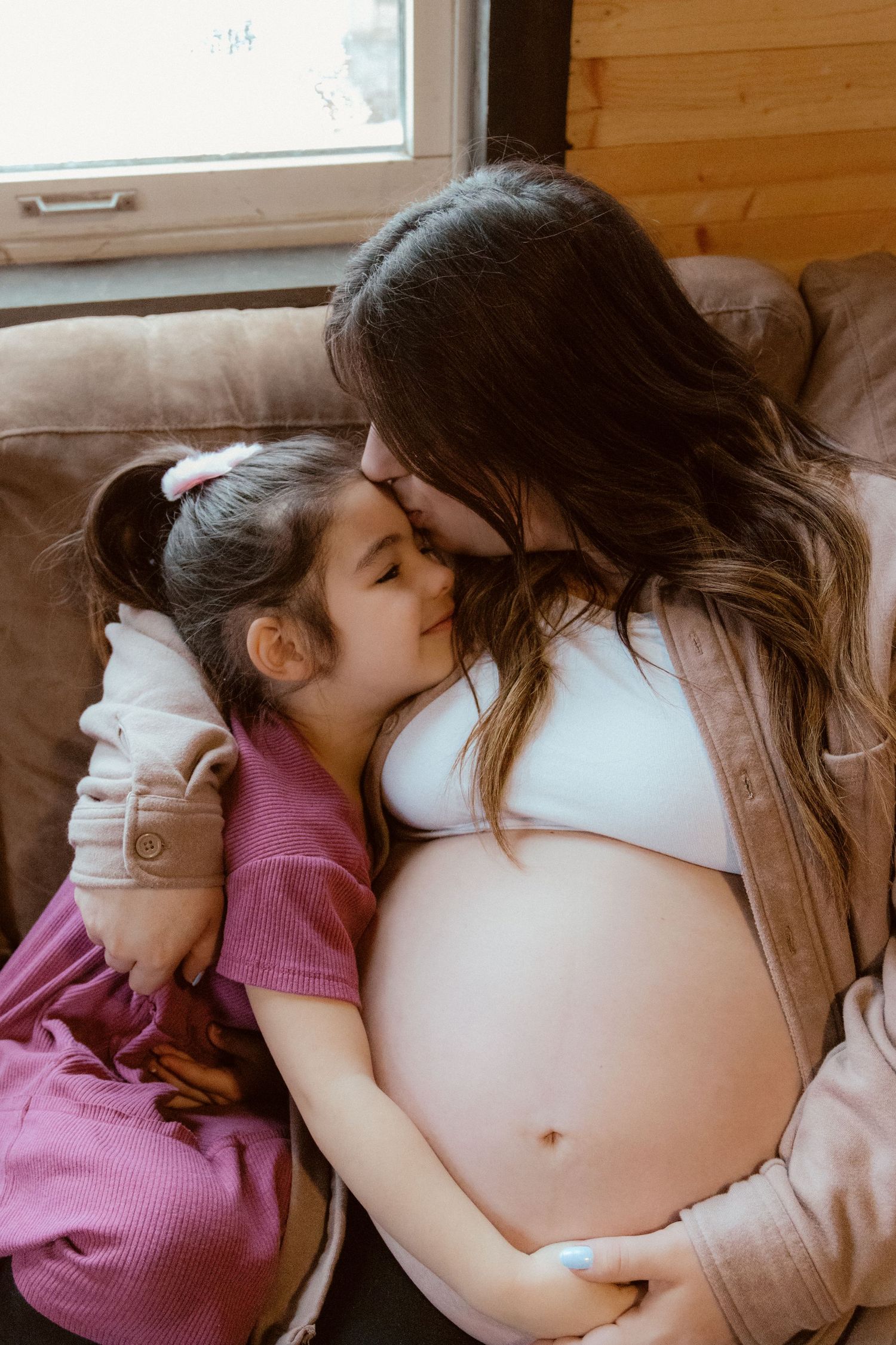 A tender moment between a parent and child as they cuddle on a couch, showing a pregnant belly.