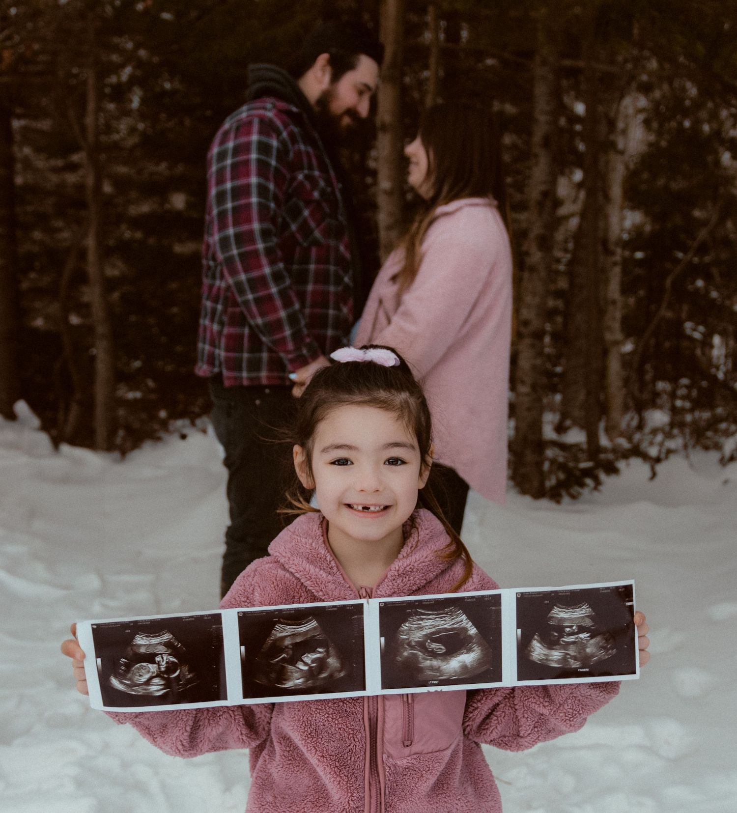 A winter family photo showing ultrasound images being held in the snowy outdoors.