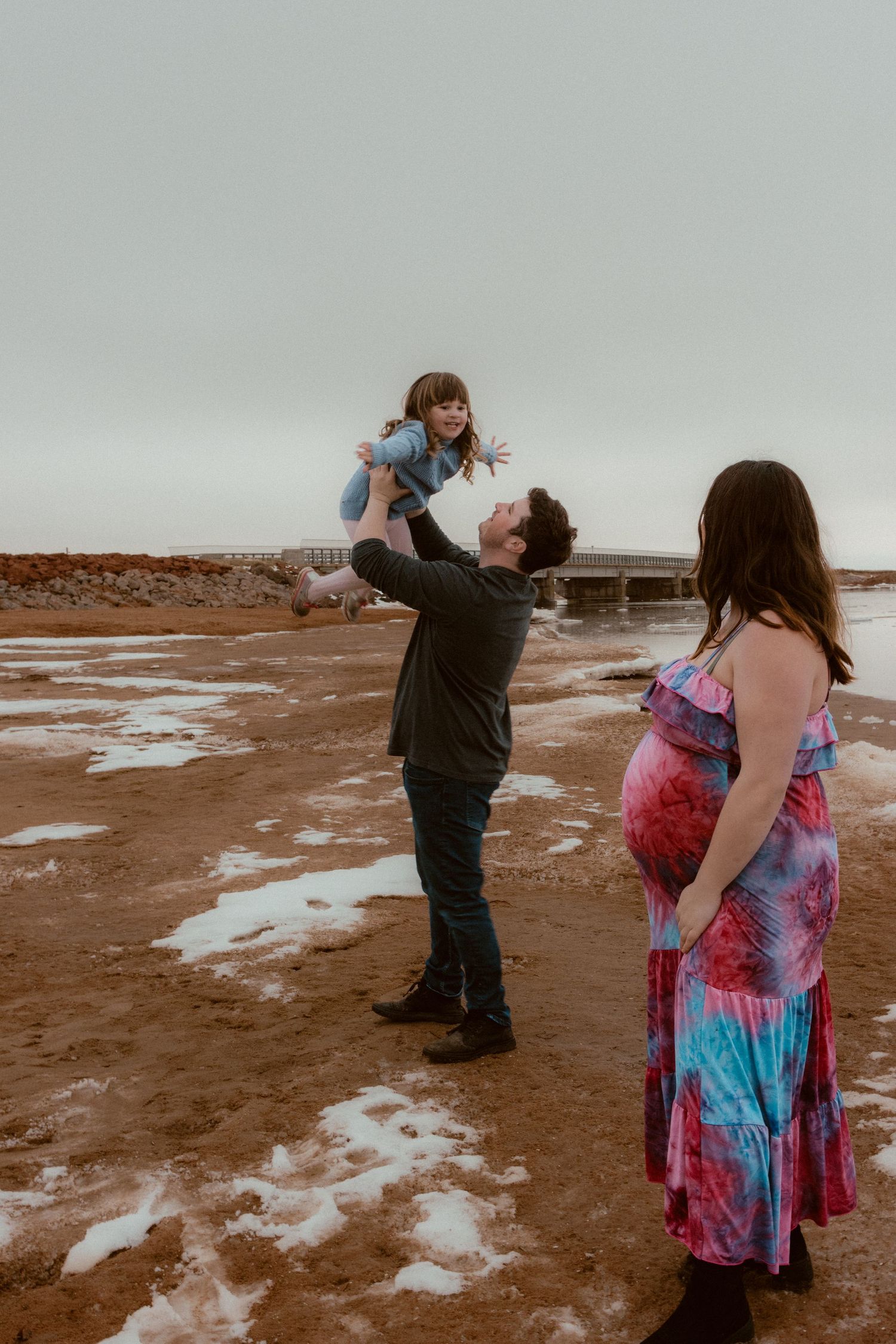 A family plays together on a beach with patches of snow visible on the ground.