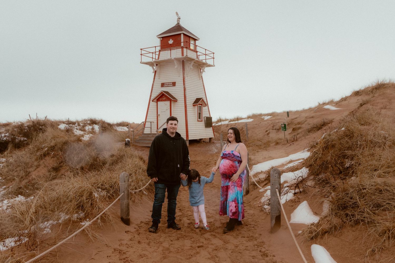 A family stands together in front of a historic lighthouse on a winter day.