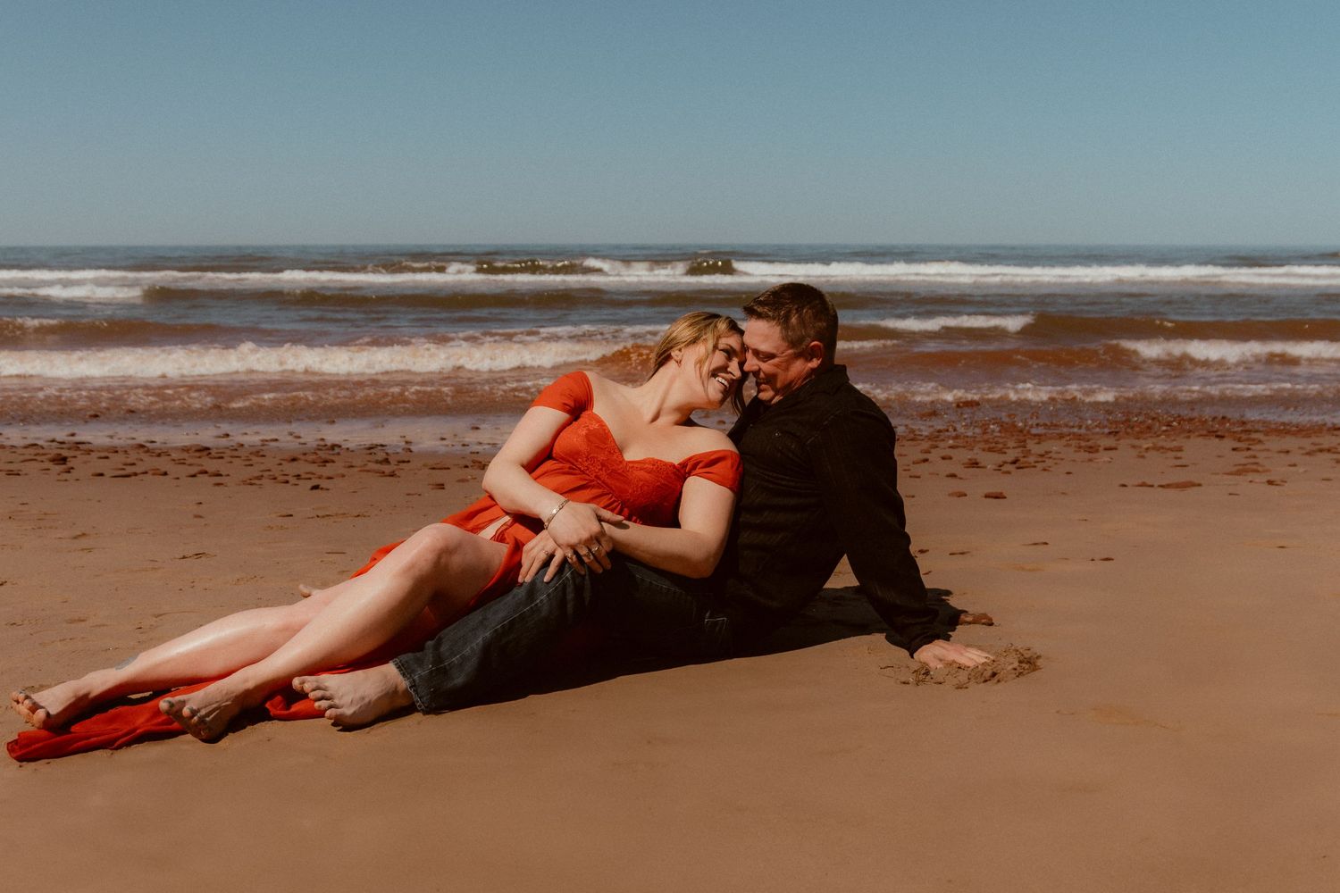A couple relaxes together on a sandy beach near the ocean.