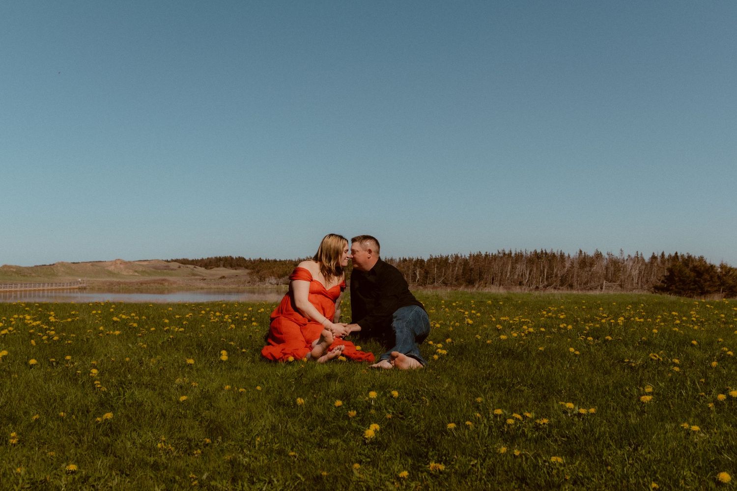 A couple sits together in a green field on a sunny summer day.