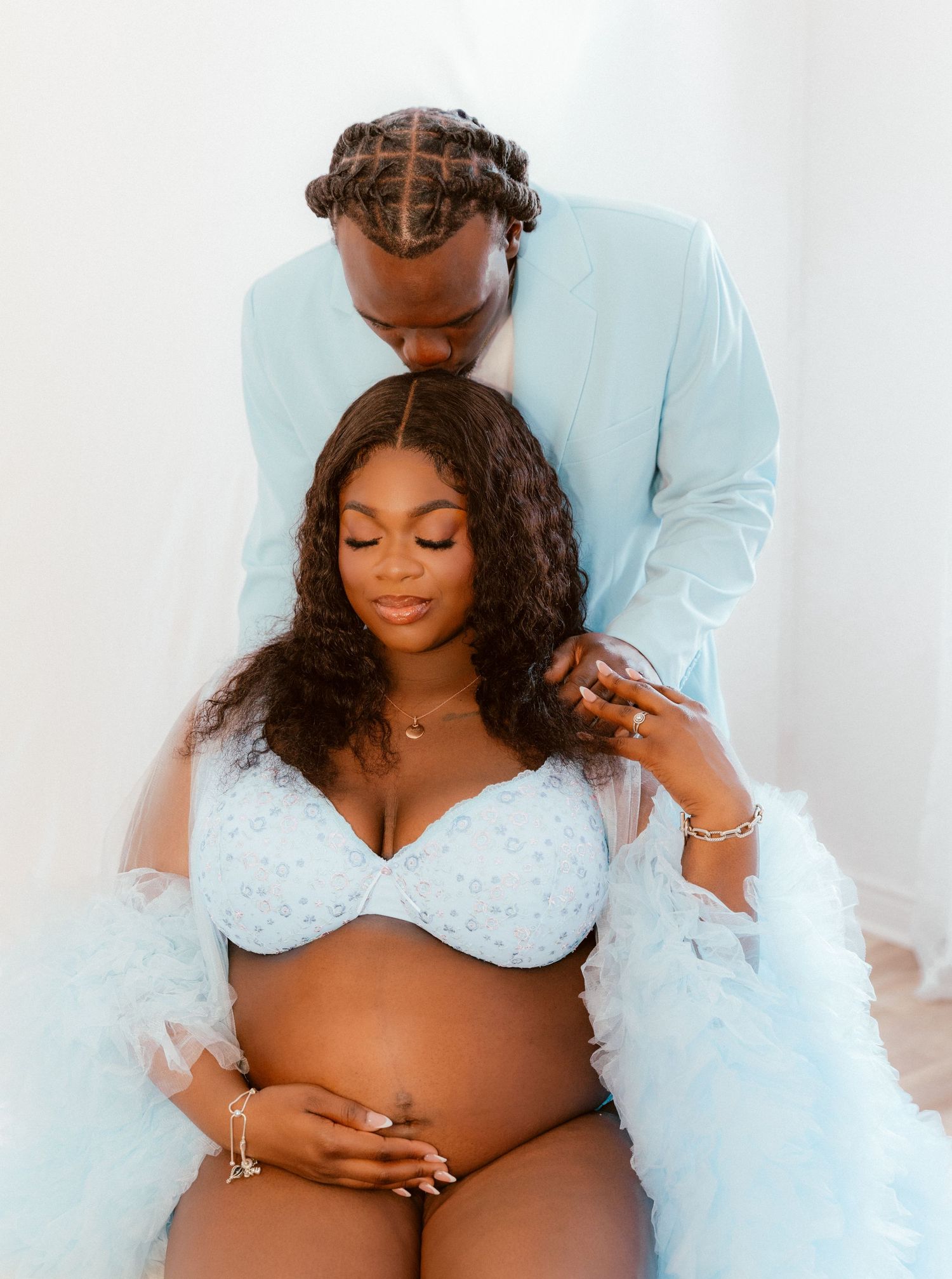 Intimate maternity photo shoot featuring a couple in soft white outfits against a light background.