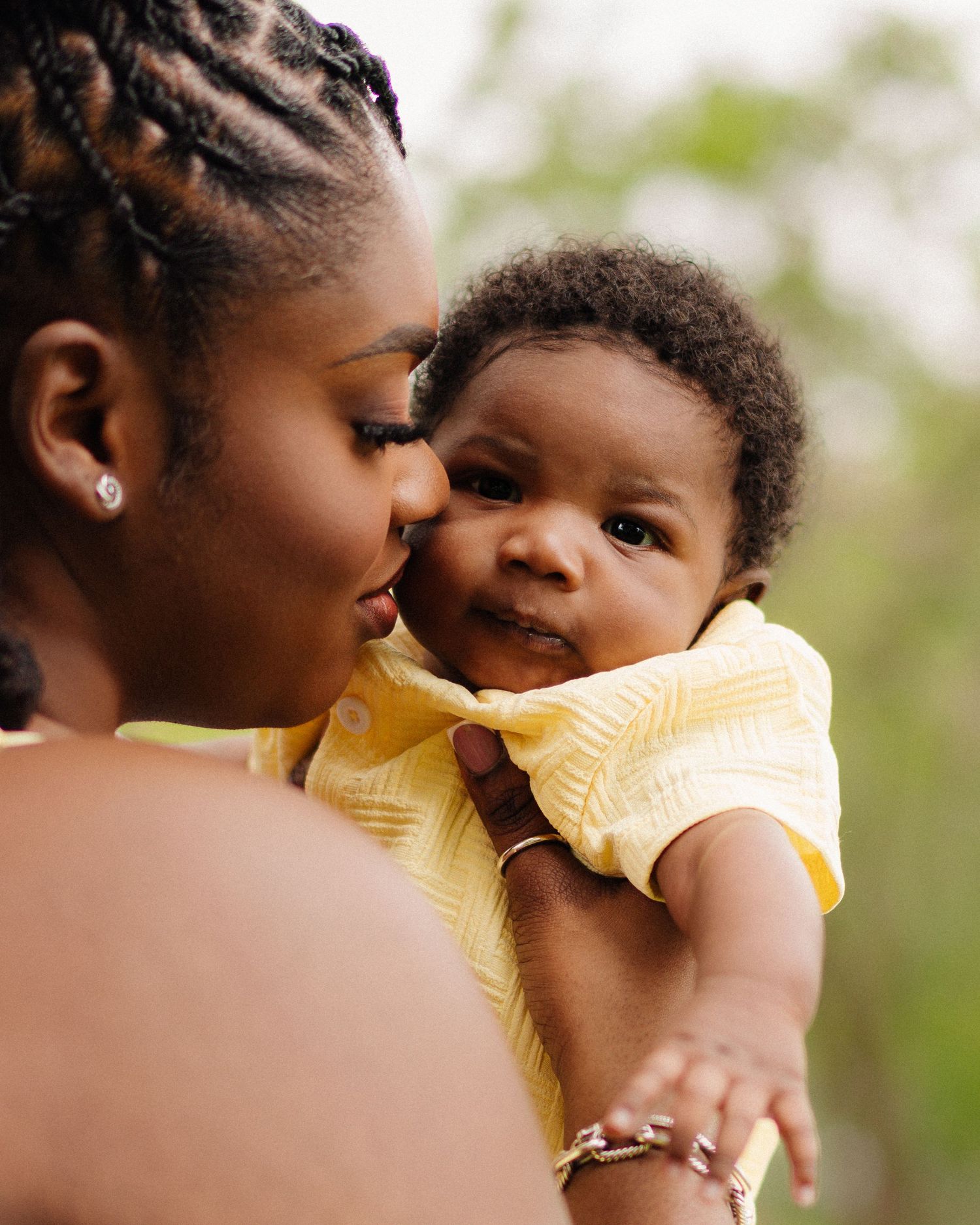 A tender moment between parent and baby wearing a yellow outfit captured in soft natural light outdoors.