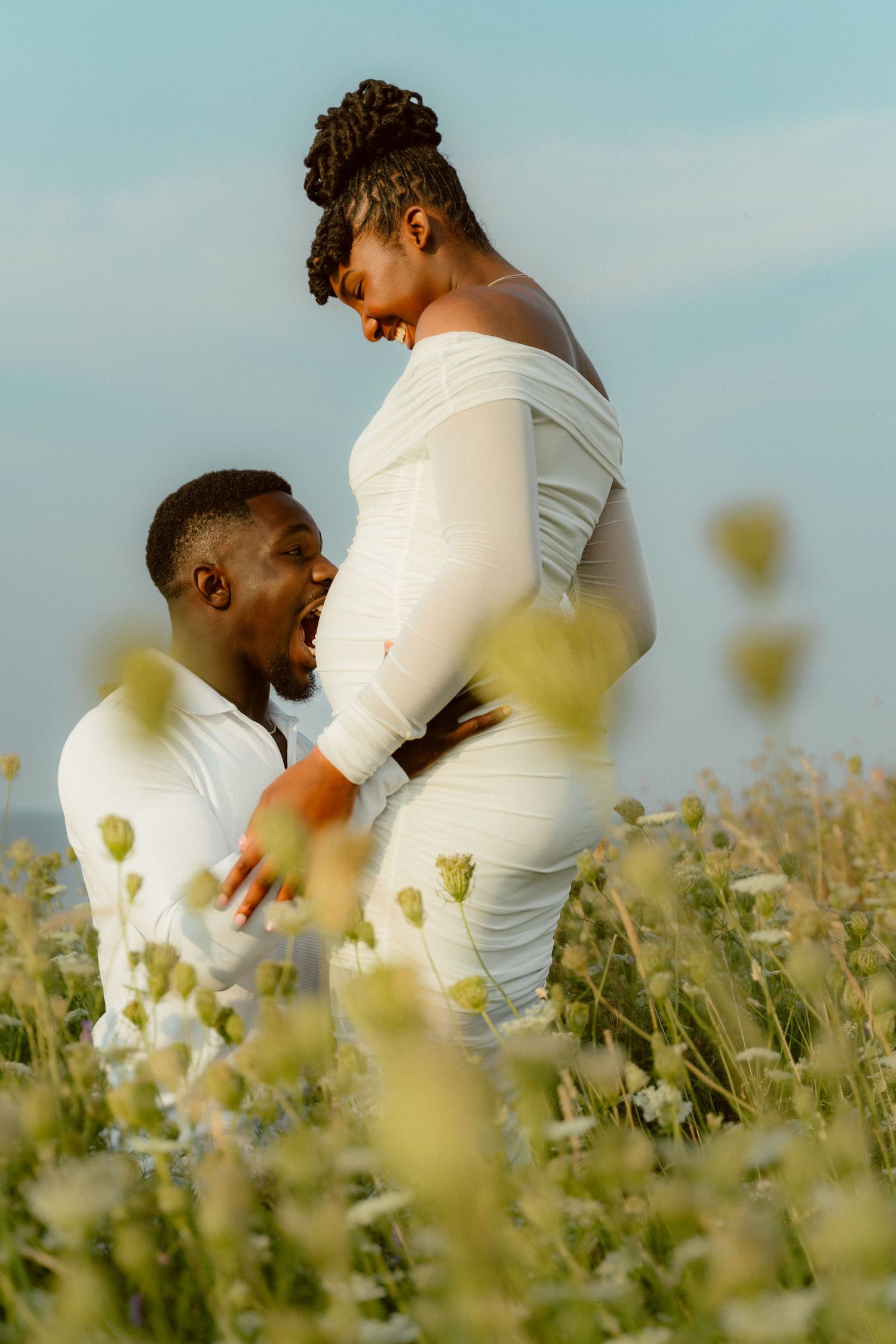 Intimate maternity moment captured in field of wildflowers during golden hour.
