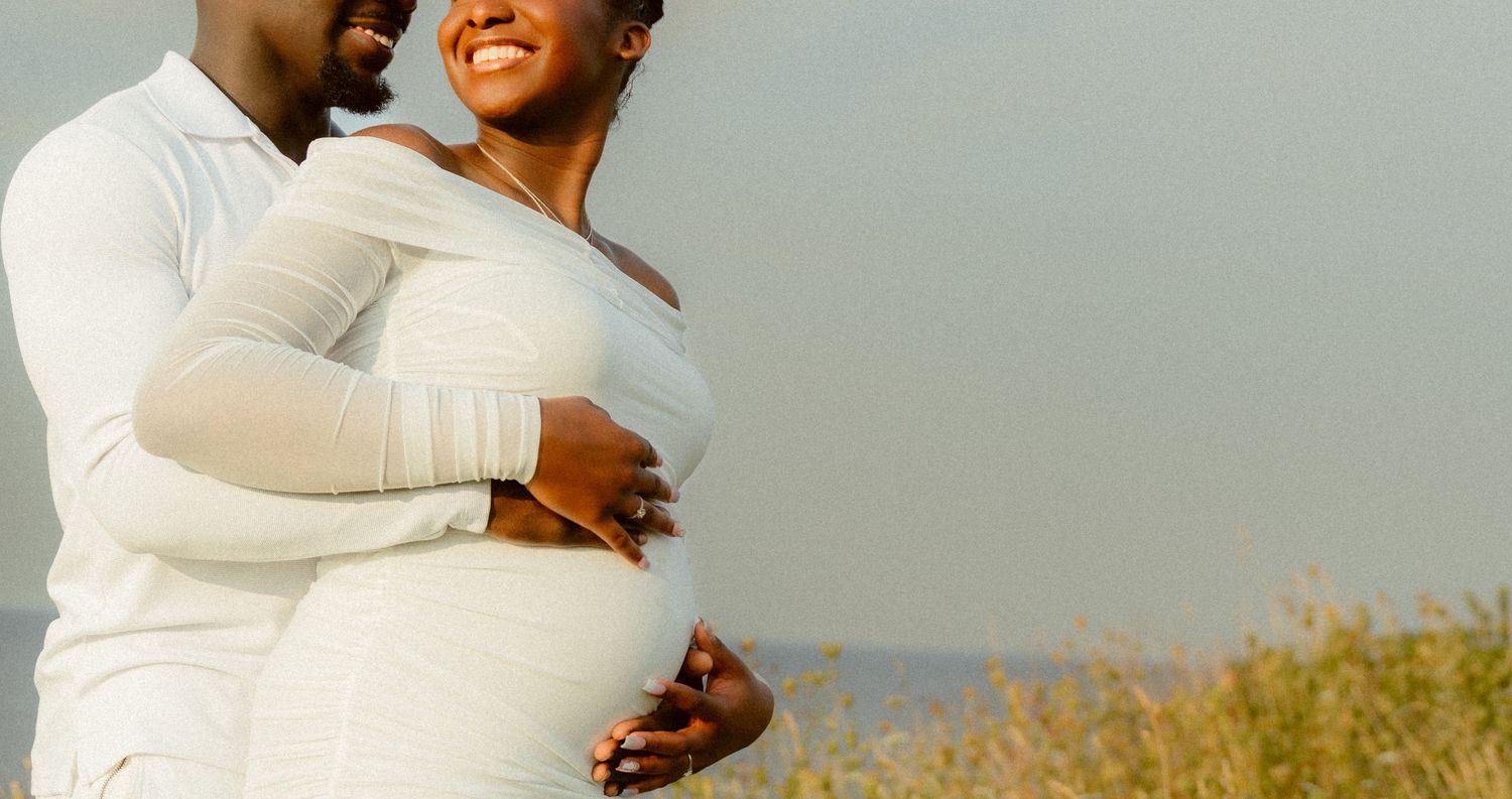 A tender moment captured between a couple wearing white outfits against a soft sky background.