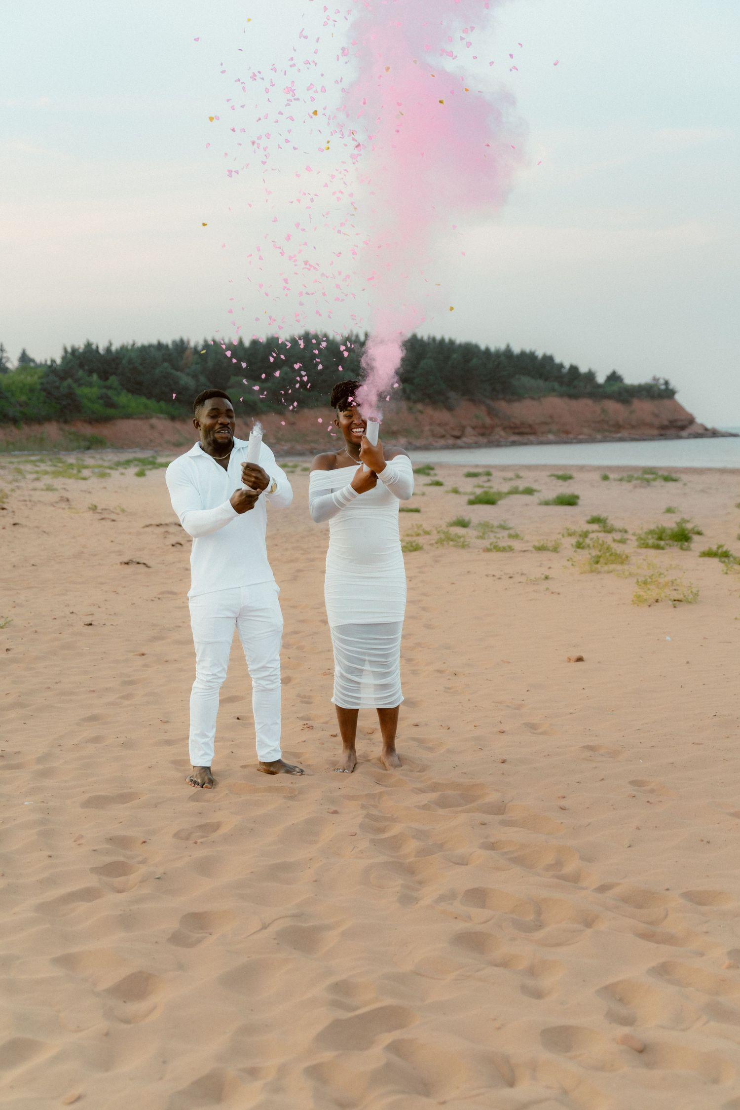 Couple celebrates with pink smoke reveal on sandy beach during sunset.