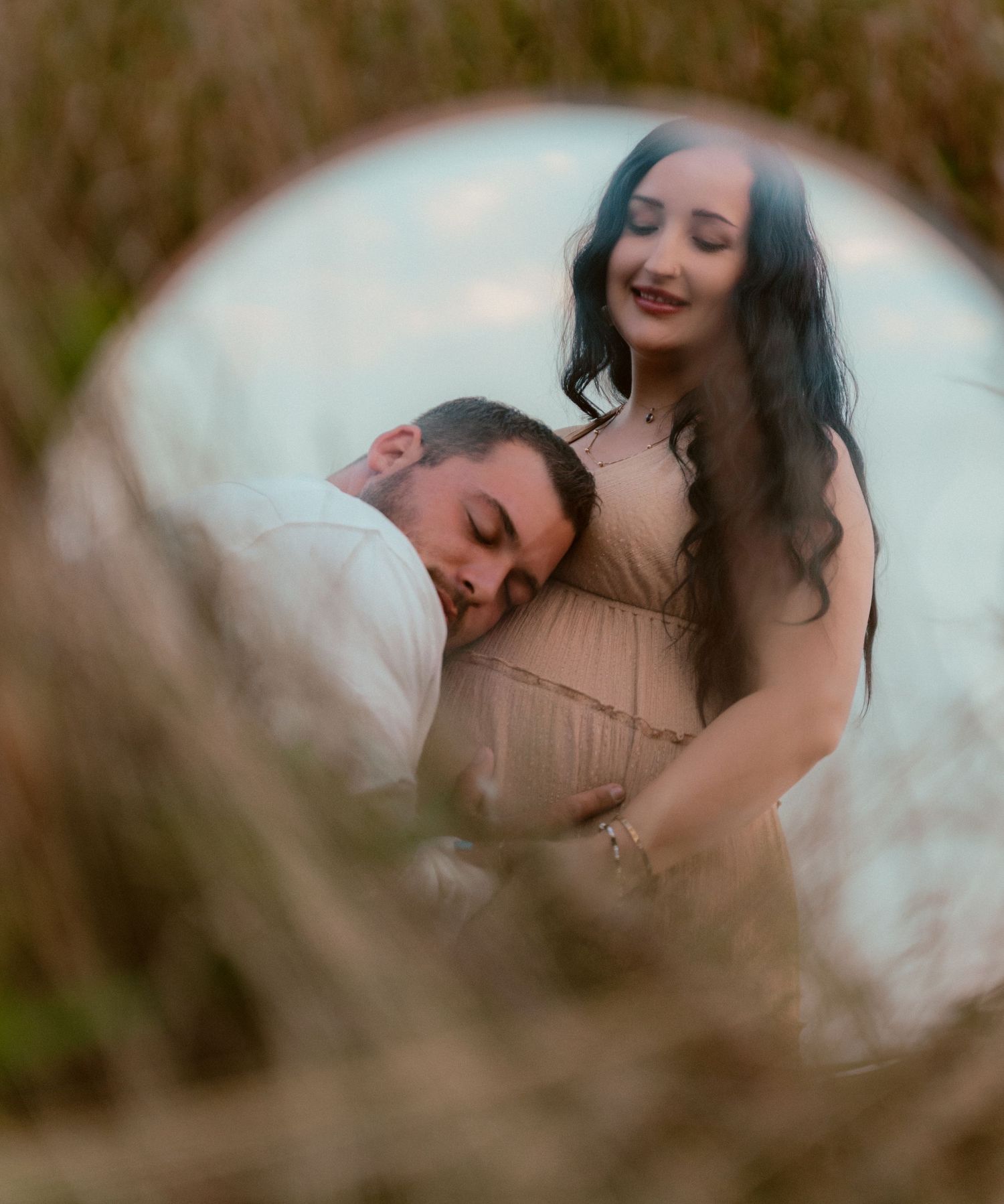 An intimate maternity photo captured through soft circular framing in nature.