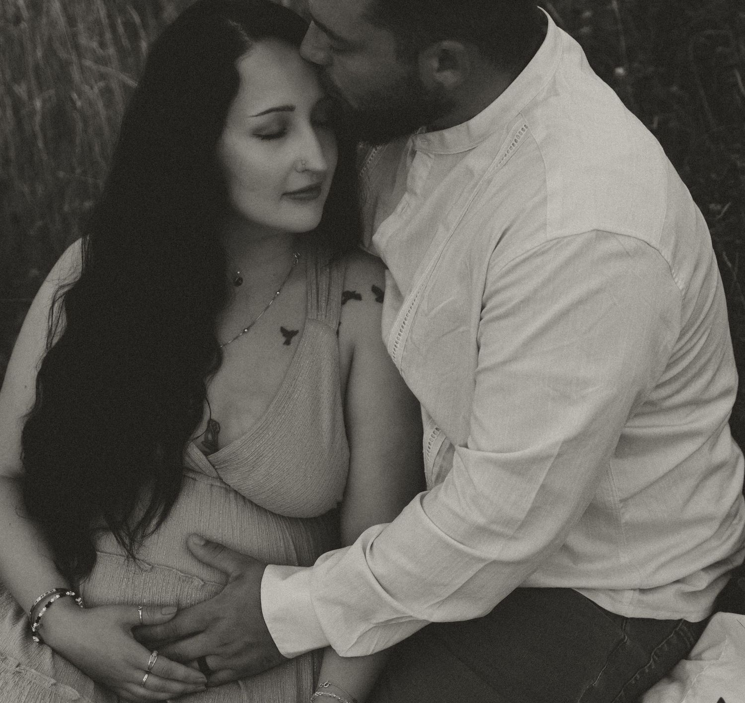 A romantic black and white maternity photo showing a tender moment outdoors.