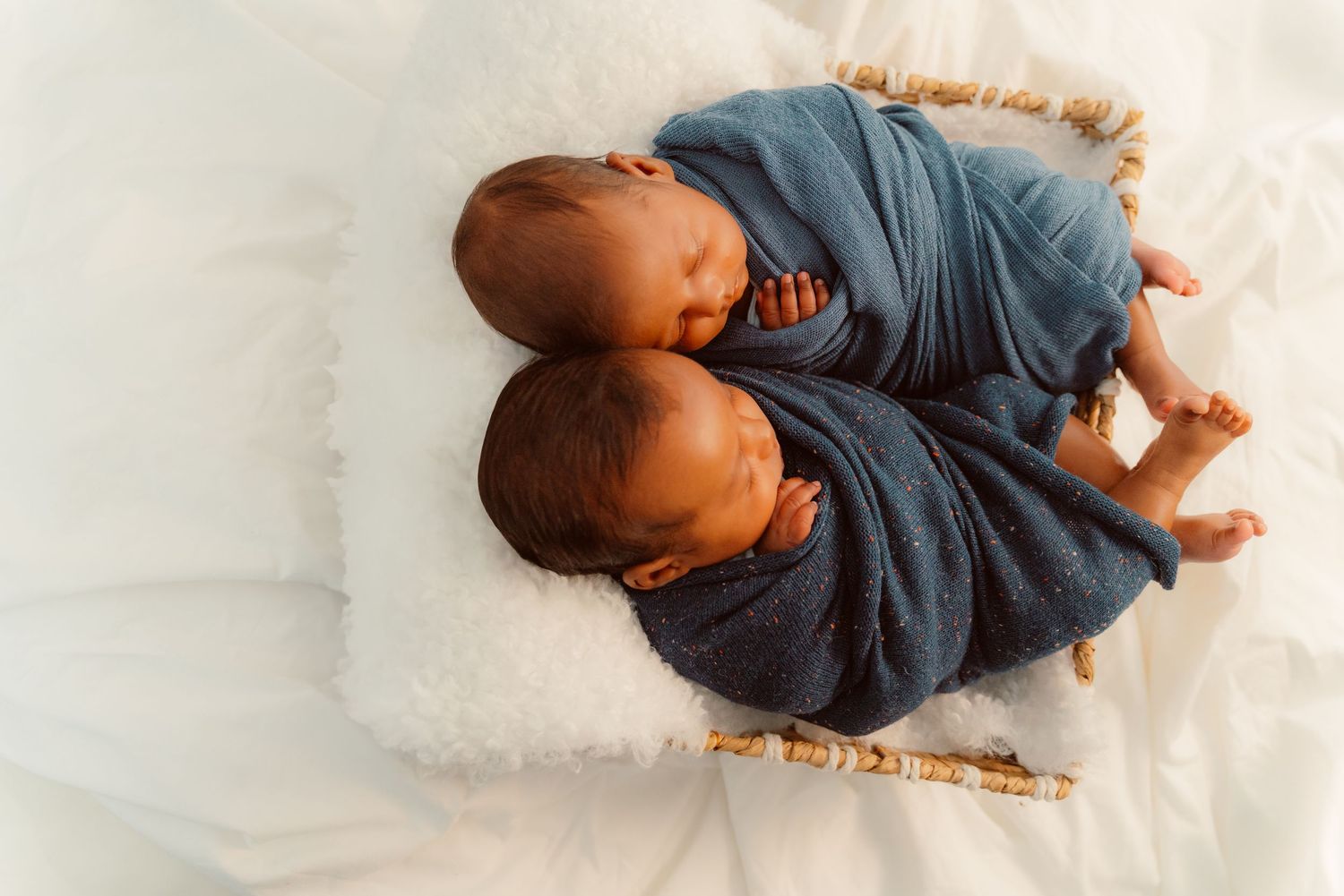 Two babies wrapped in blue blankets lying beside each other in a peaceful sleeping position on a white surface.